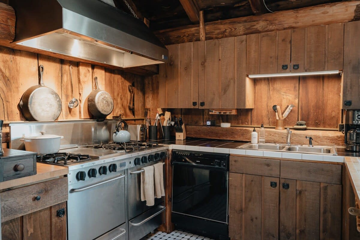 Detailed view of the kitchen's cooking area, featuring a professional-grade stainless steel range with a large hood, wooden backsplash, and cast iron pans hanging on the wall.