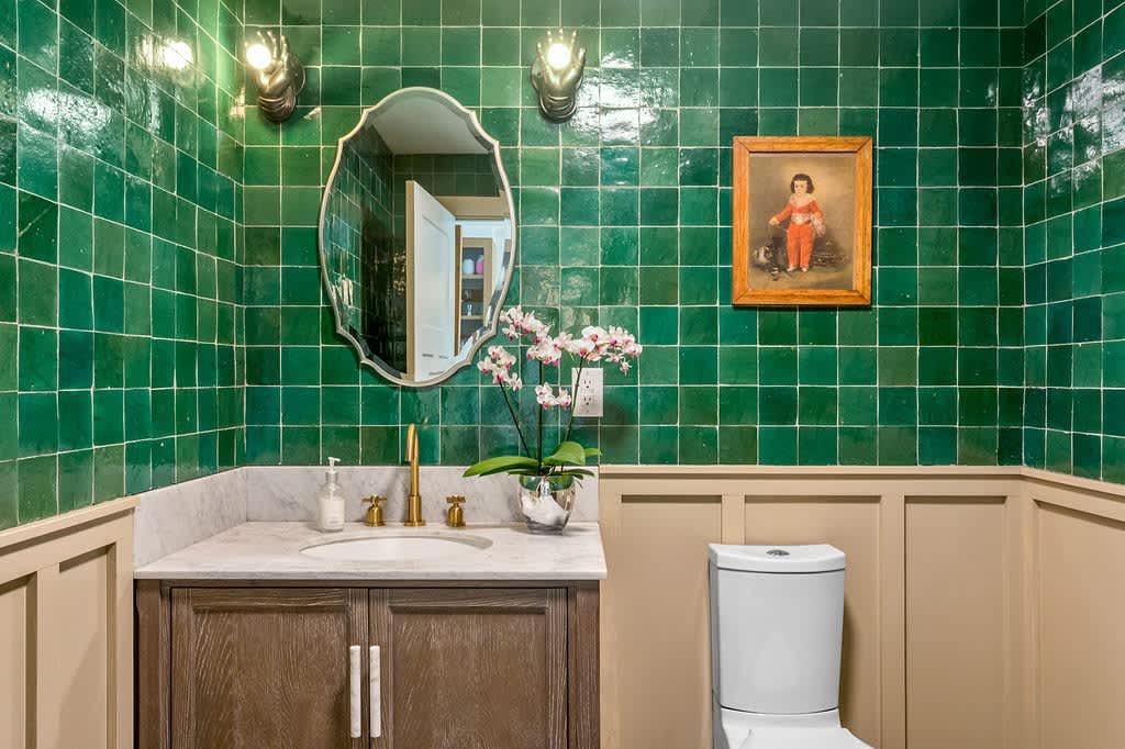 Vibrant powder room with emerald green square tiles covering the upper walls, a dark wood vanity with a marble countertop and gold faucet, and a decorative mirror, creating a bold and eclectic style.