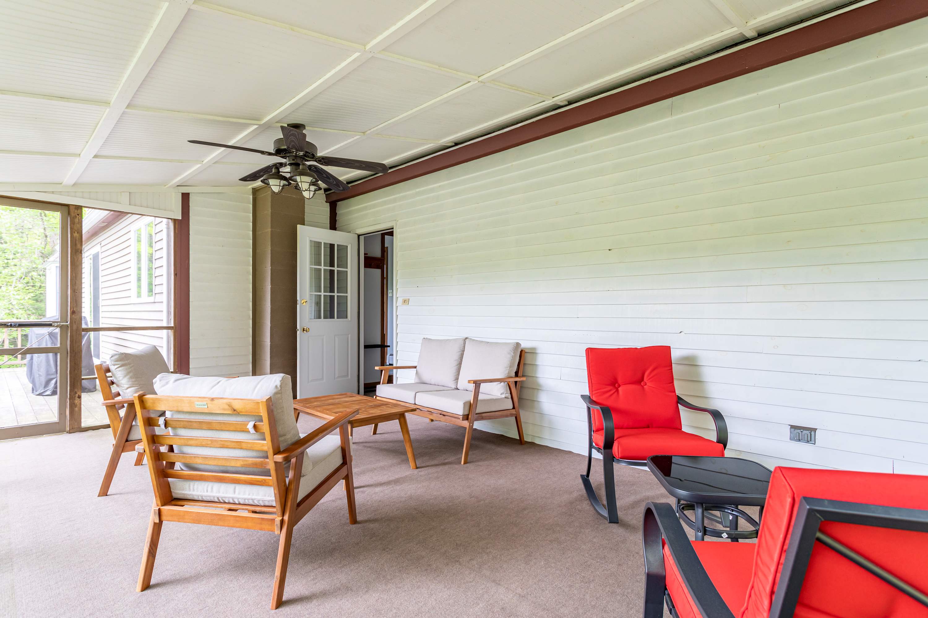 Screened-in porch furnished with comfortable outdoor seating, including a sofa, armchairs, and a coffee table, with a ceiling fan overhead.