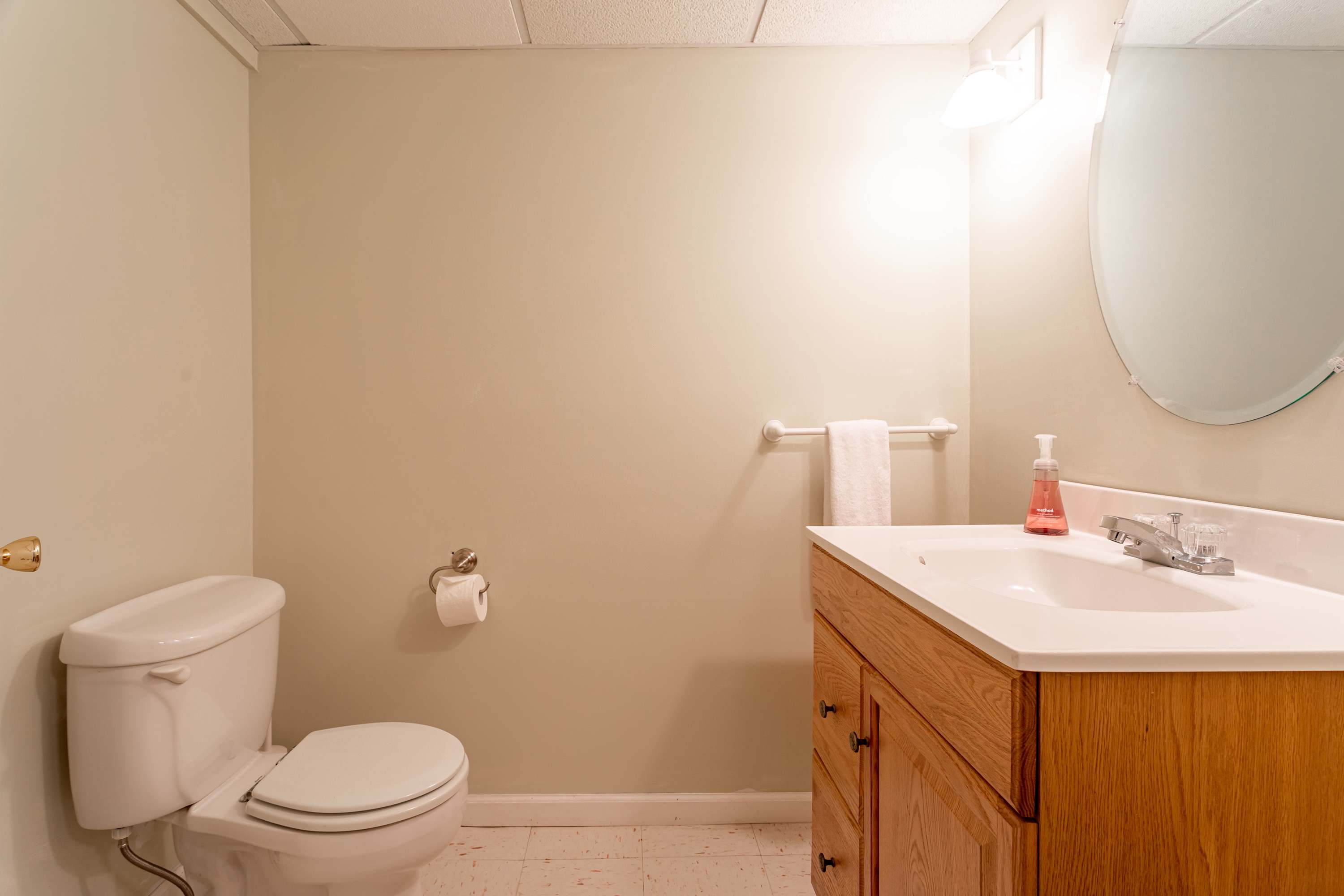 Simple half bathroom with light beige walls, a light wood vanity with a white sink, a toilet, and an oval mirror above the sink.
