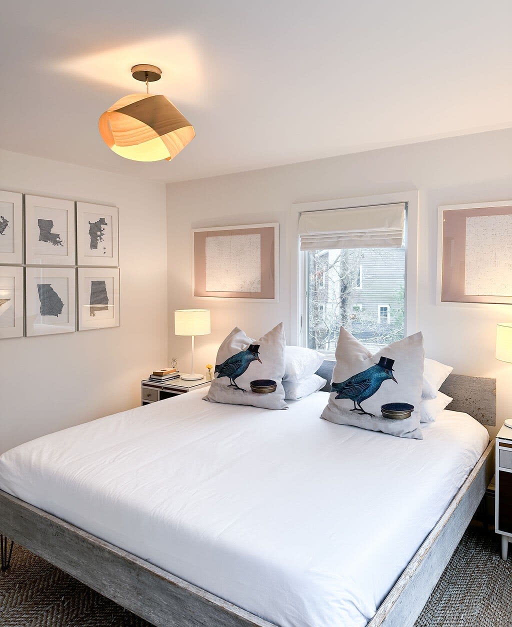 Cozy bedroom featuring a large bed with white linens and bird-patterned pillows, flanked by bedside tables with lamps, and a gallery wall of framed art above the headboard.