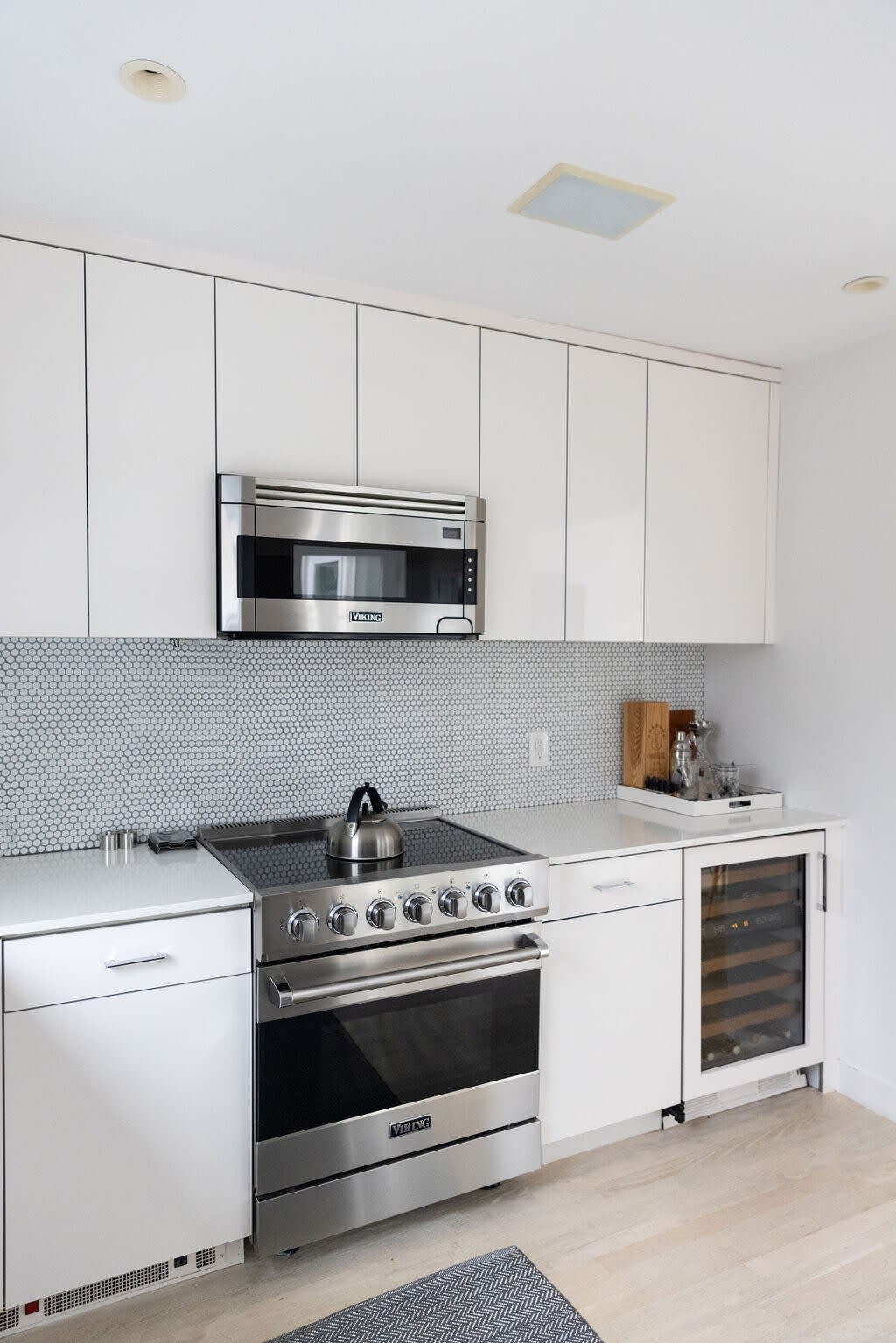 A close-up of the modern kitchen highlights the stainless steel Viking range and matching overhead microwave, set against a gray penny tile backsplash. White flat-panel cabinets and light countertops complete the clean, contemporary look.