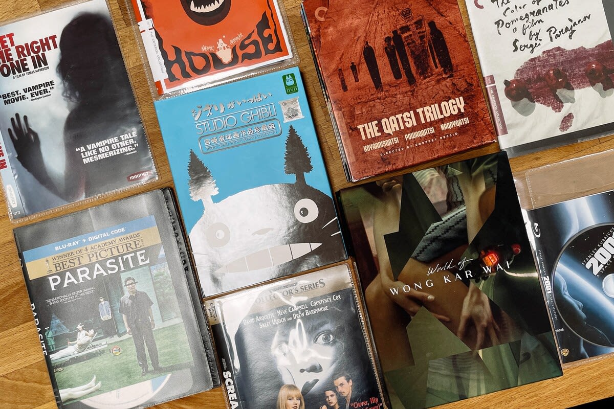 A close-up shot displays a collection of movie DVDs and Blu-rays, including titles like "Parasite," "Studio Ghibli," and "World of Wong Kar Wai," laid out on a wooden surface.