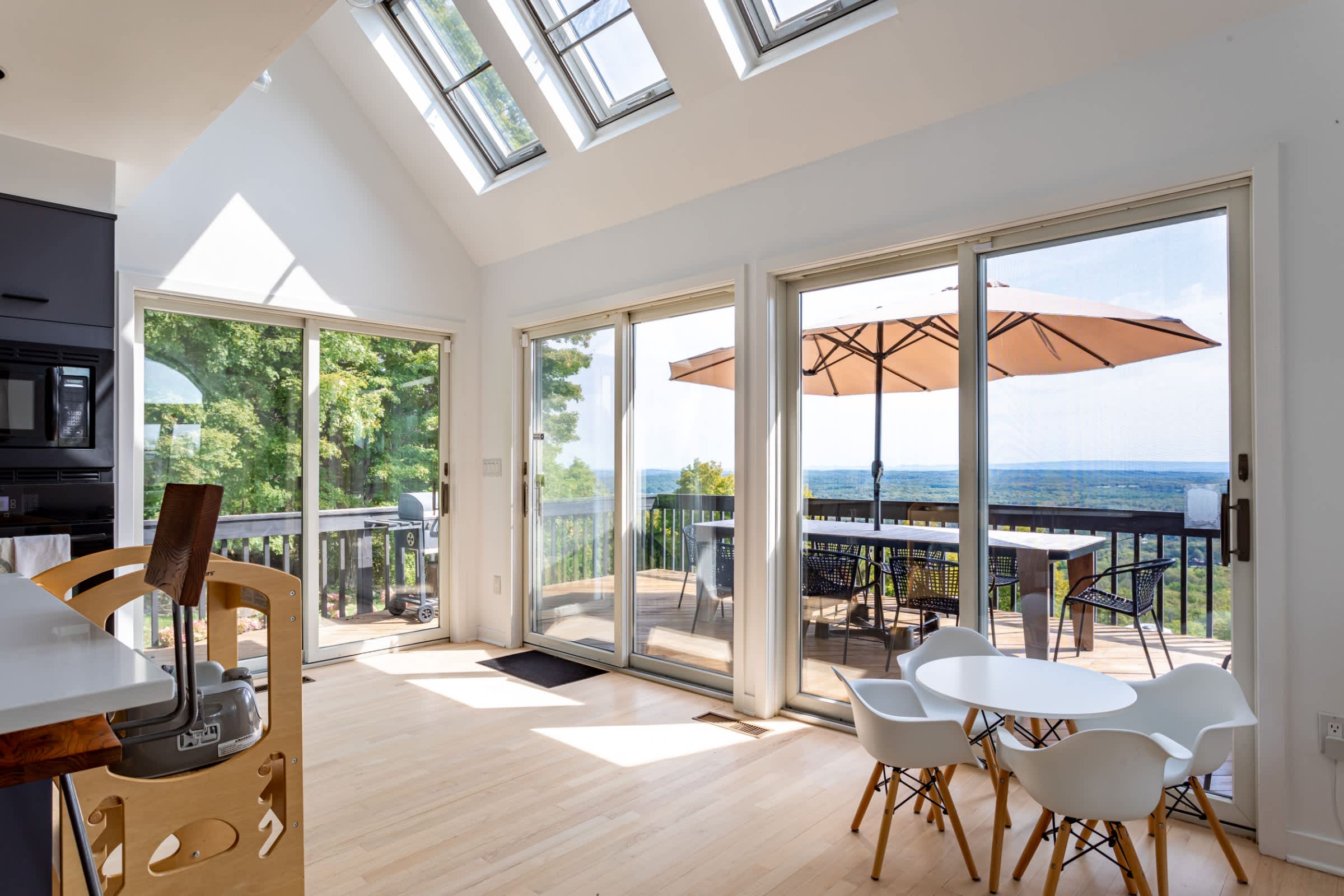 Bright dining area with light hardwood floors and a small white dining table, featuring large sliding glass doors that open to a deck with expansive valley views, complemented by multiple skylights.