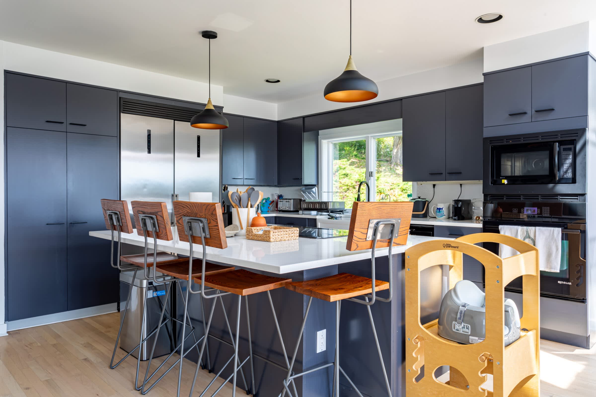 Contemporary kitchen featuring dark grey flat-panel cabinetry, a large white quartz island with seating for four, stainless steel appliances, and modern pendant lighting.