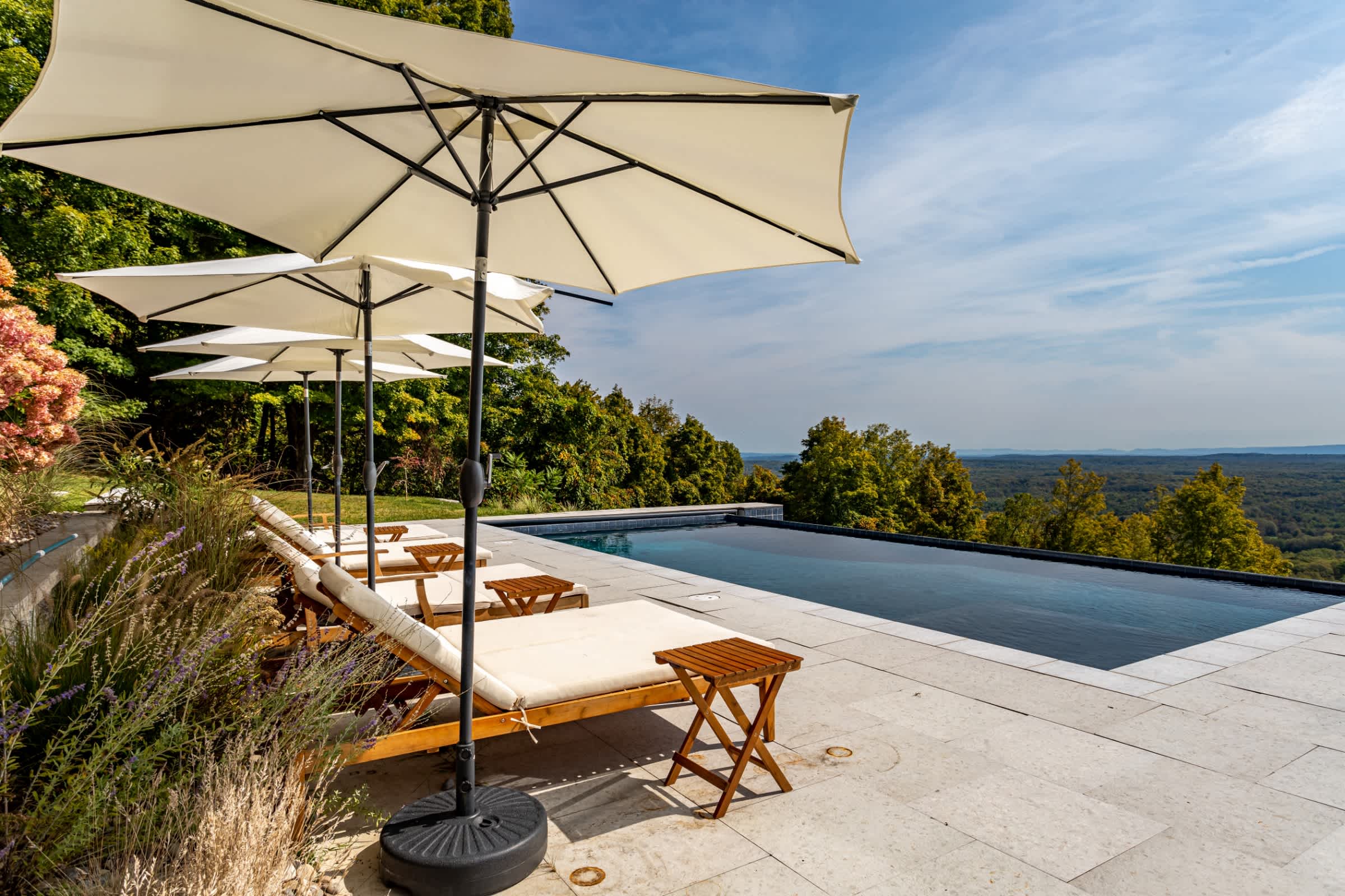 Close-up of the pool deck with several wooden lounge chairs and white umbrellas, positioned to enjoy the stunning infinity pool and panoramic mountain views.