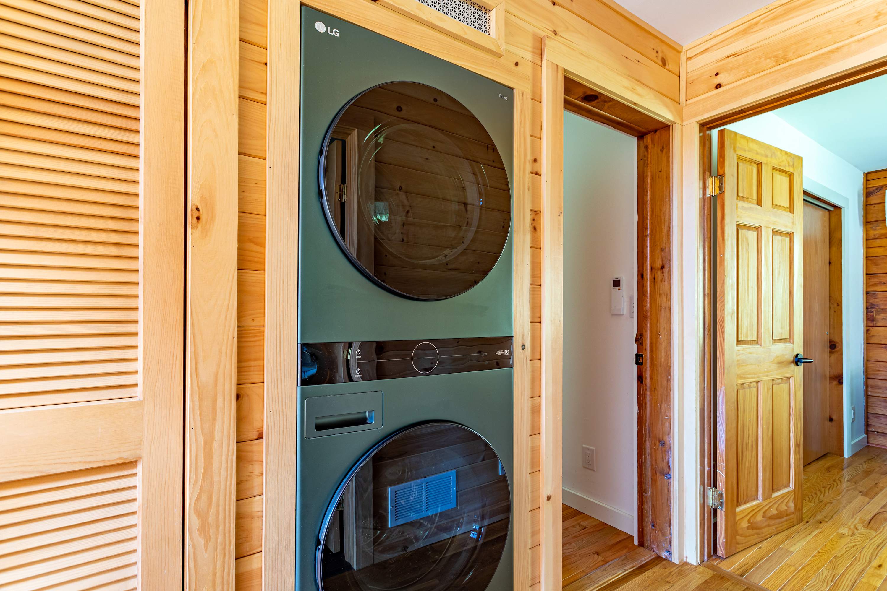 Dedicated laundry area with a modern stacked LG washer and dryer unit, set within a natural wood-paneled alcove. Adjacent wooden doors lead to other rooms.