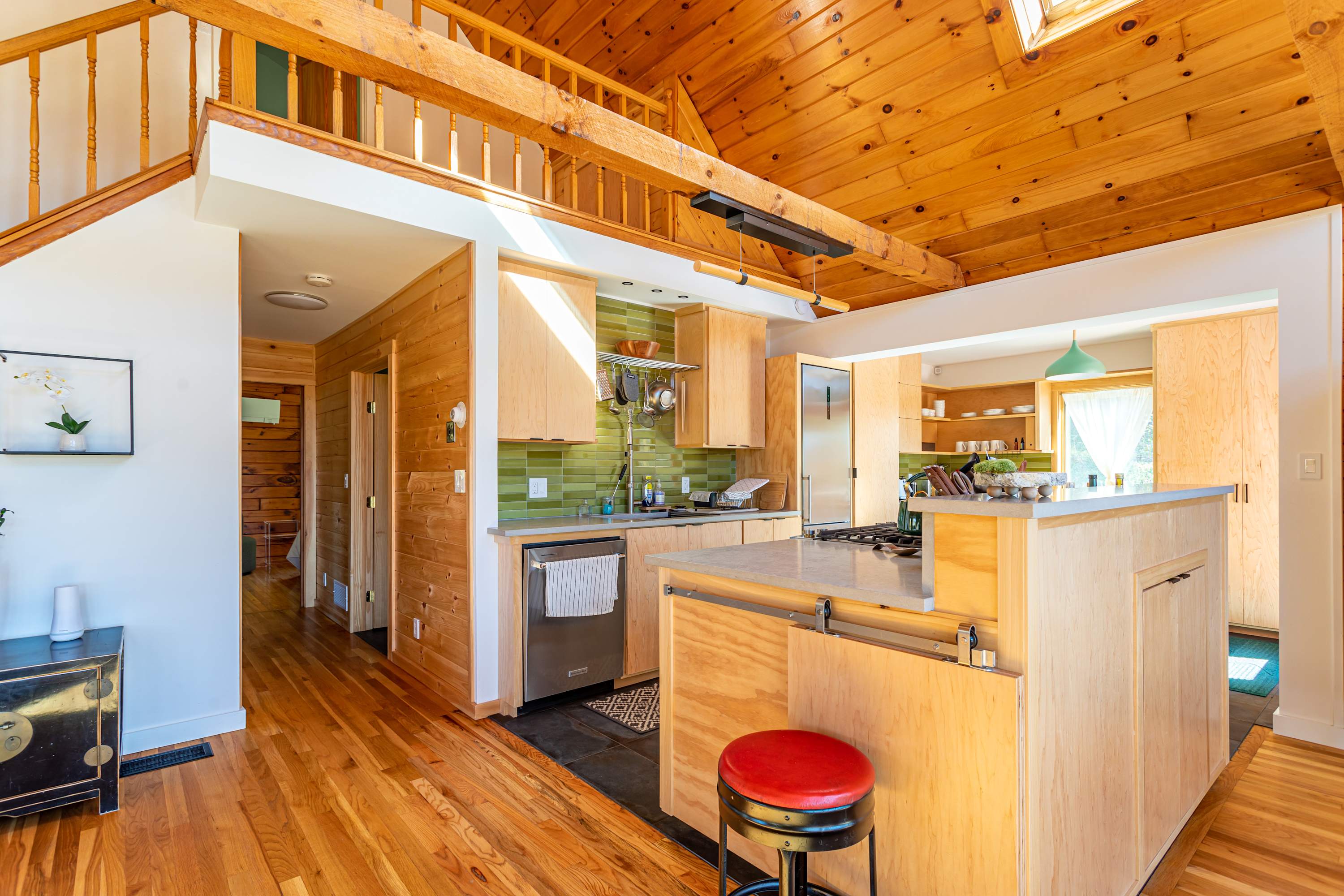 Modern kitchen with light wood cabinetry, a large island with a light countertop, stainless steel appliances, and a green subway tile backsplash, all integrated into an open-concept space with hardwood floors.