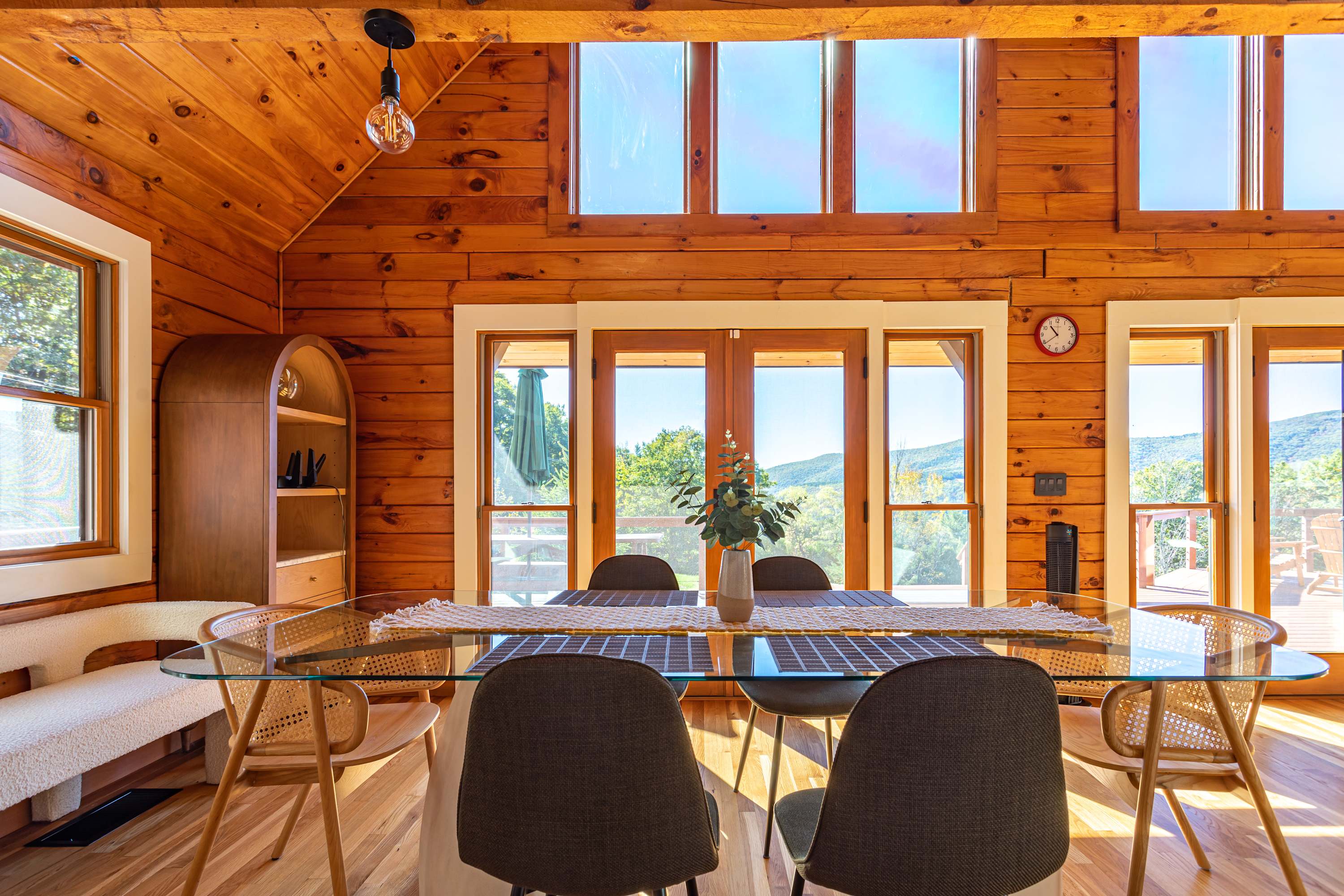 Elegant dining area featuring a glass-top dining table with modern chairs, set against a backdrop of large windows and glass doors that offer panoramic mountain views, all within a wood-paneled room.