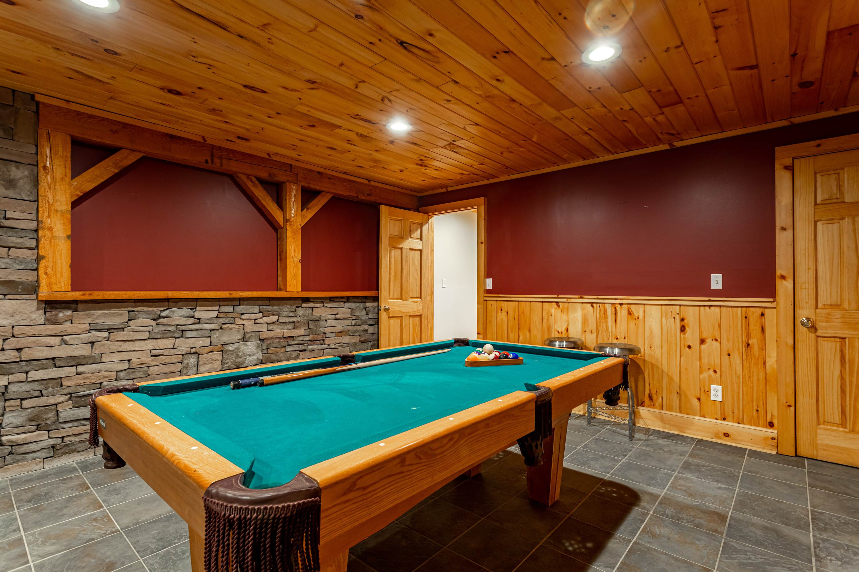 Game room with a wooden ceiling and wainscoting, a stone accent wall, and a full-sized pool table, creating a cozy recreational space.