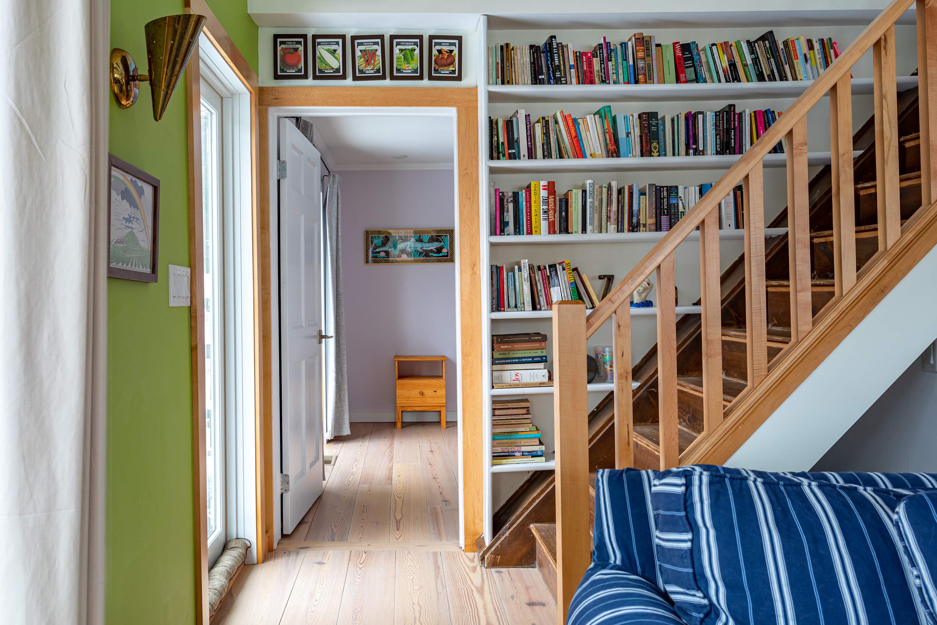 A hallway with lime green walls and hardwood floors connects the living area to a bedroom, featuring a wooden staircase with built-in bookshelves and a glimpse of a light lavender room beyond.