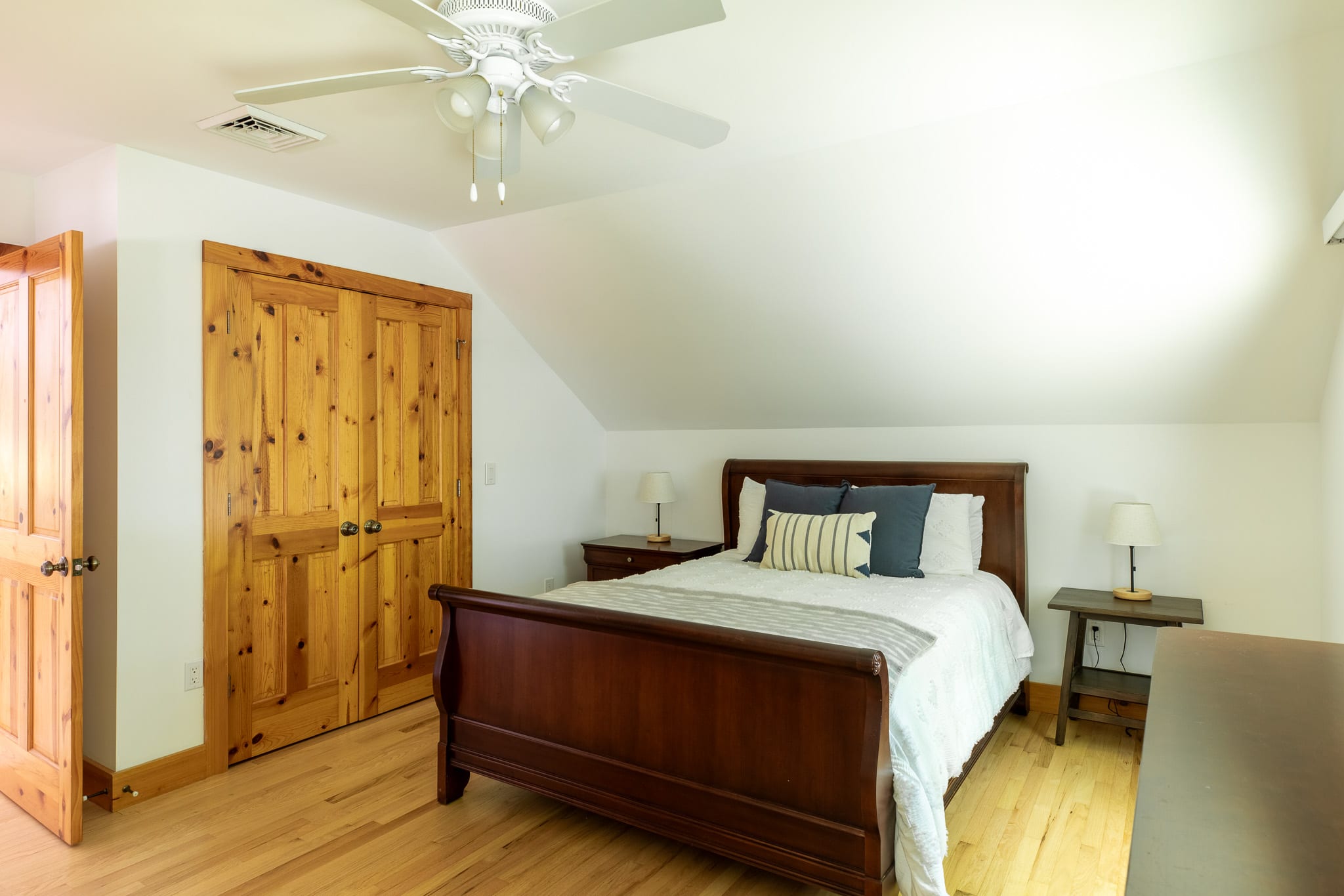 Another view of the bedroom, highlighting the dark wood sleigh bed, matching furniture, and natural wood bi-fold closet doors, with a ceiling fan overhead and hardwood floors throughout.