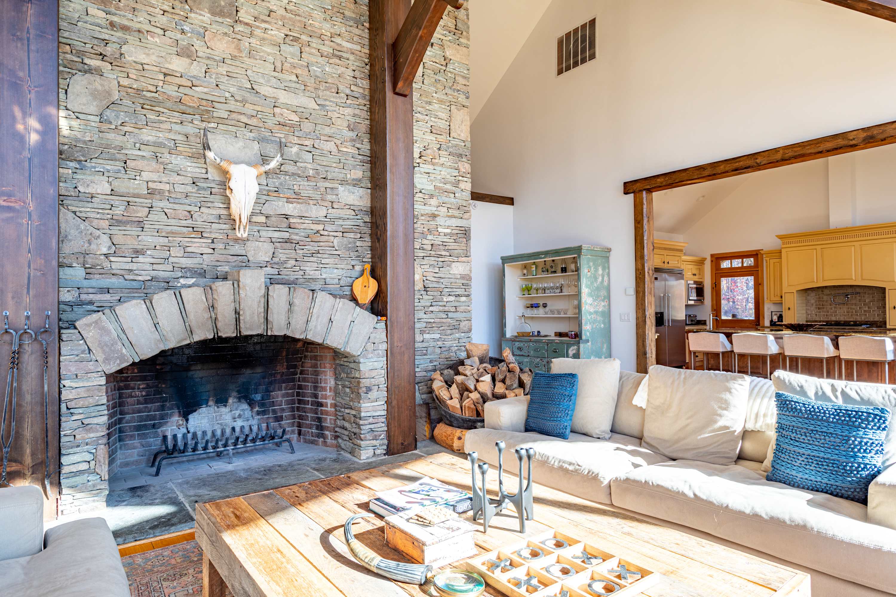 A close-up view of the rustic stone fireplace in the living room, featuring a large arched opening, a metal grate, and a skull decoration on the mantel, with stacked firewood nearby.