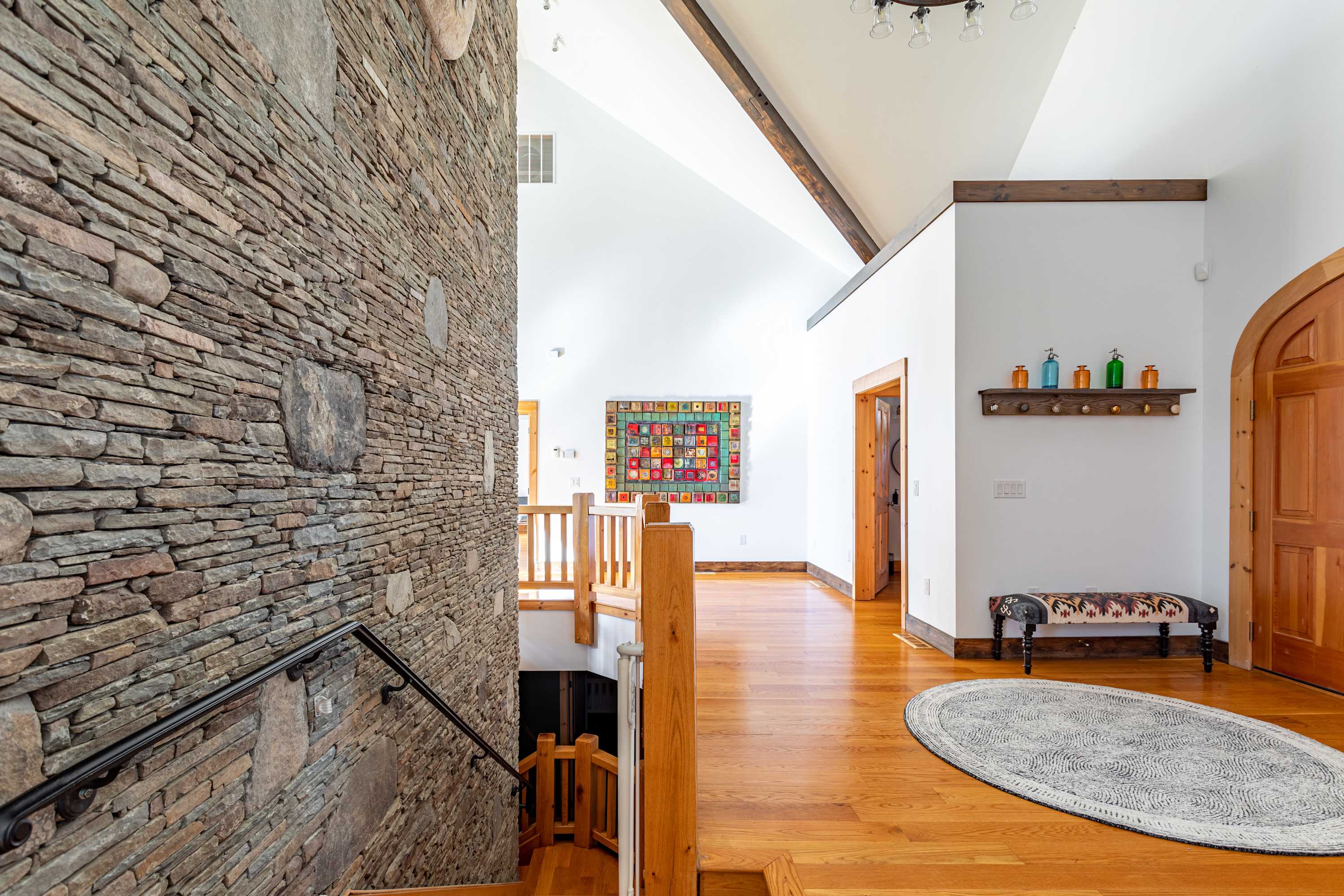 View of a grand stone wall with large natural stone accents, running alongside a wooden staircase with a matching railing, creating a rustic yet elegant transition space.