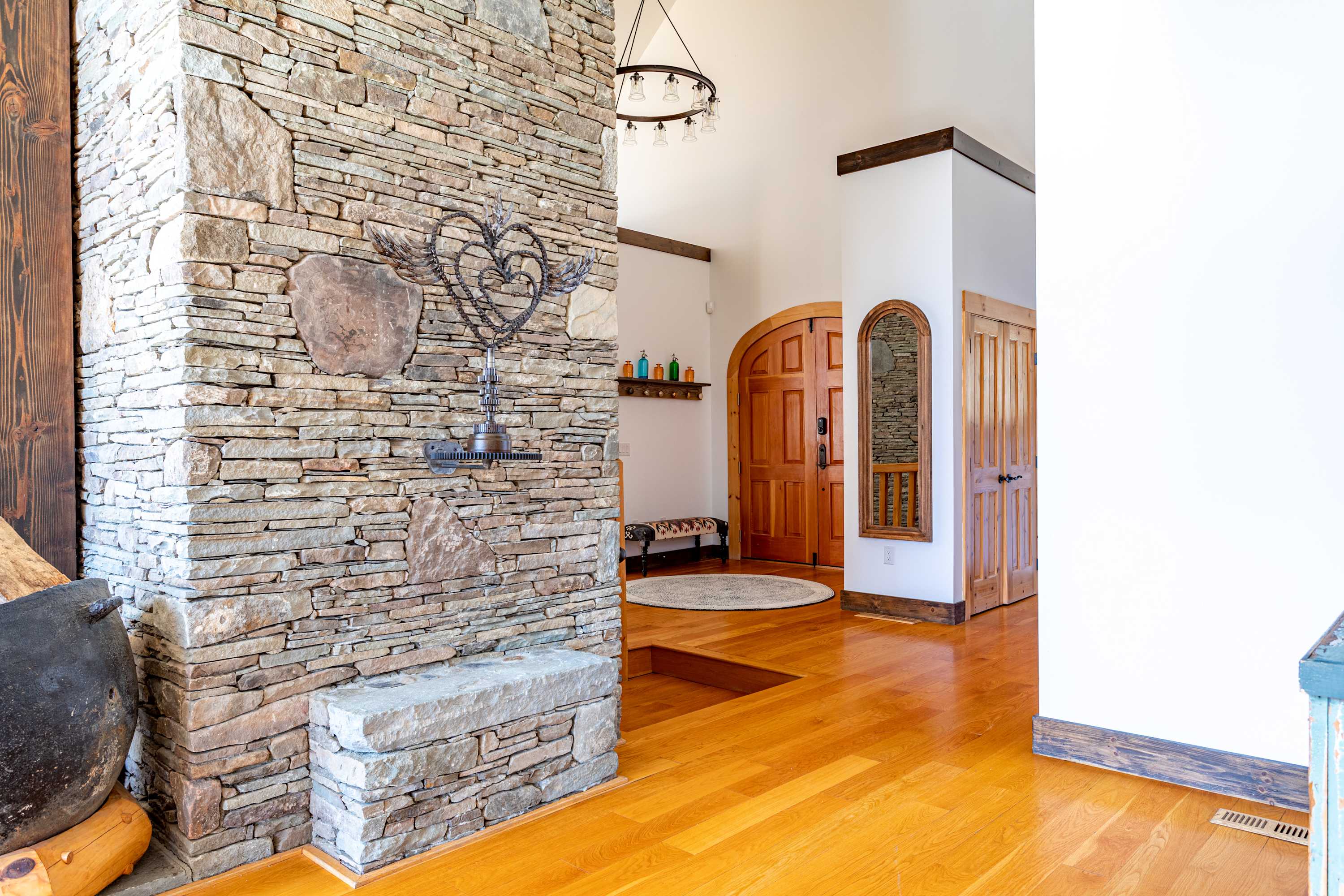 View of the stone wall extending into an open area, featuring a built-in stone bench and a large decorative pot on the floor, with the foyer entrance visible in the background.