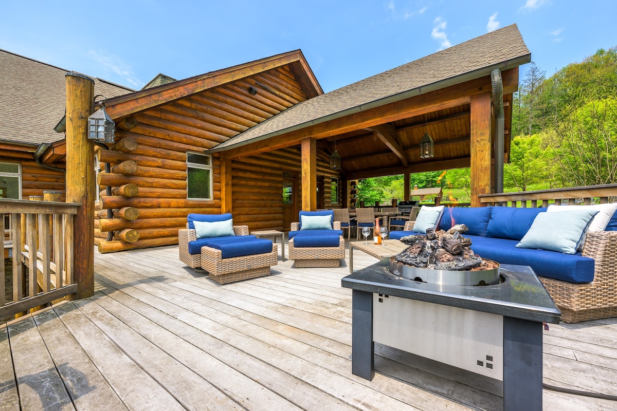 Spacious outdoor wooden deck furnished with comfortable wicker seating, blue cushions, and a modern fire pit, offering a relaxing space with views of the surrounding greenery.