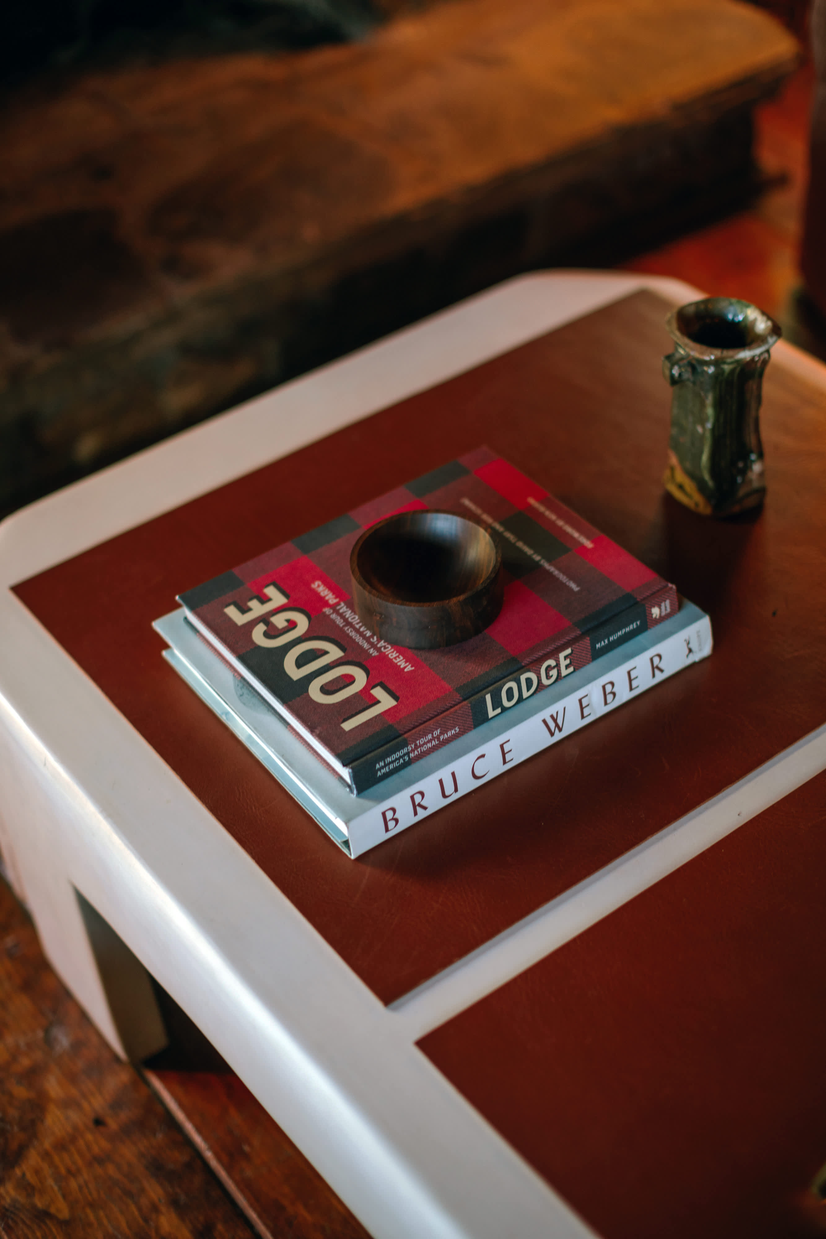 A close-up shot reveals a coffee table adorned with two books titled 'LODGE', a small wooden bowl, and a ceramic cup. The table's surface features a brown and white design, adding a touch of modern rustic to the space.