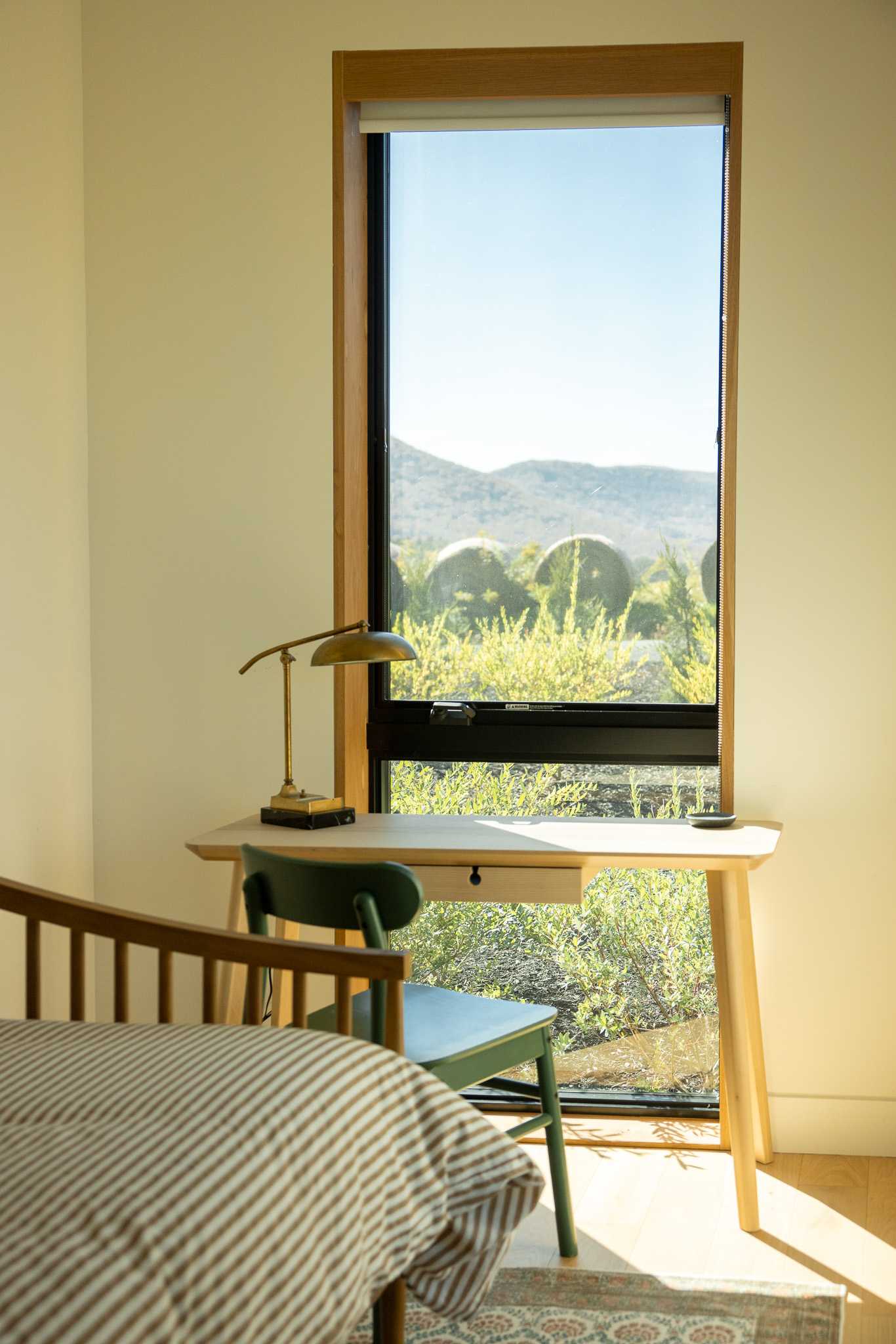 Close-up of the wooden desk and green chair in the bedroom, illuminated by natural light from a tall window showcasing a unique landscape with distant dome-like structures.