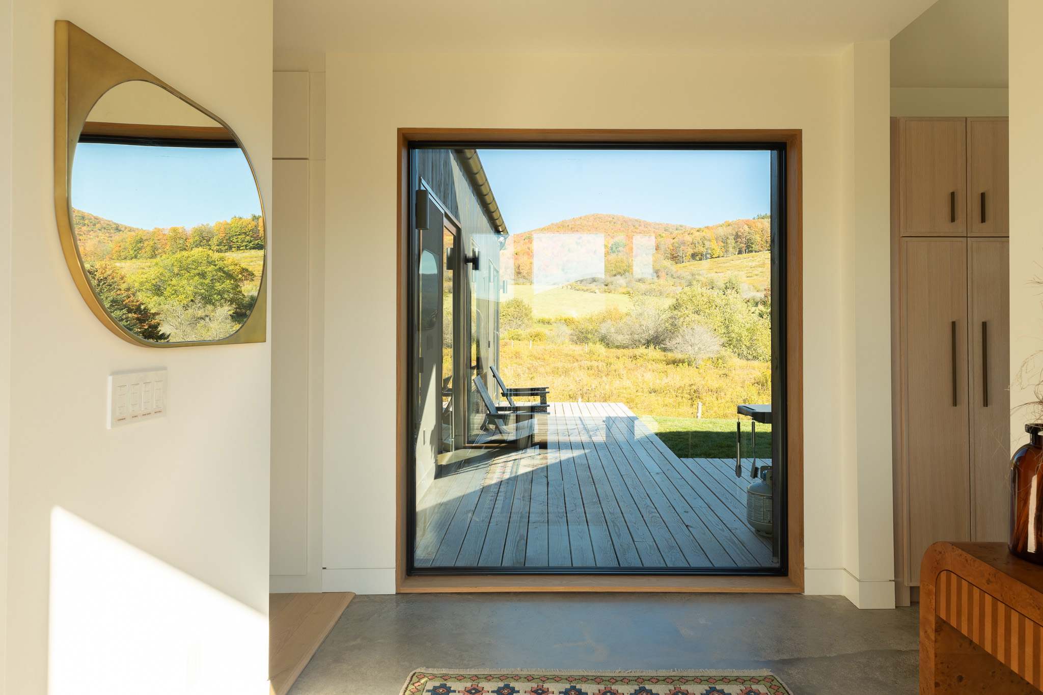 Entryway with a large floor-to-ceiling window offering a direct view of the outdoor deck and the expansive, sunny autumn landscape beyond.
