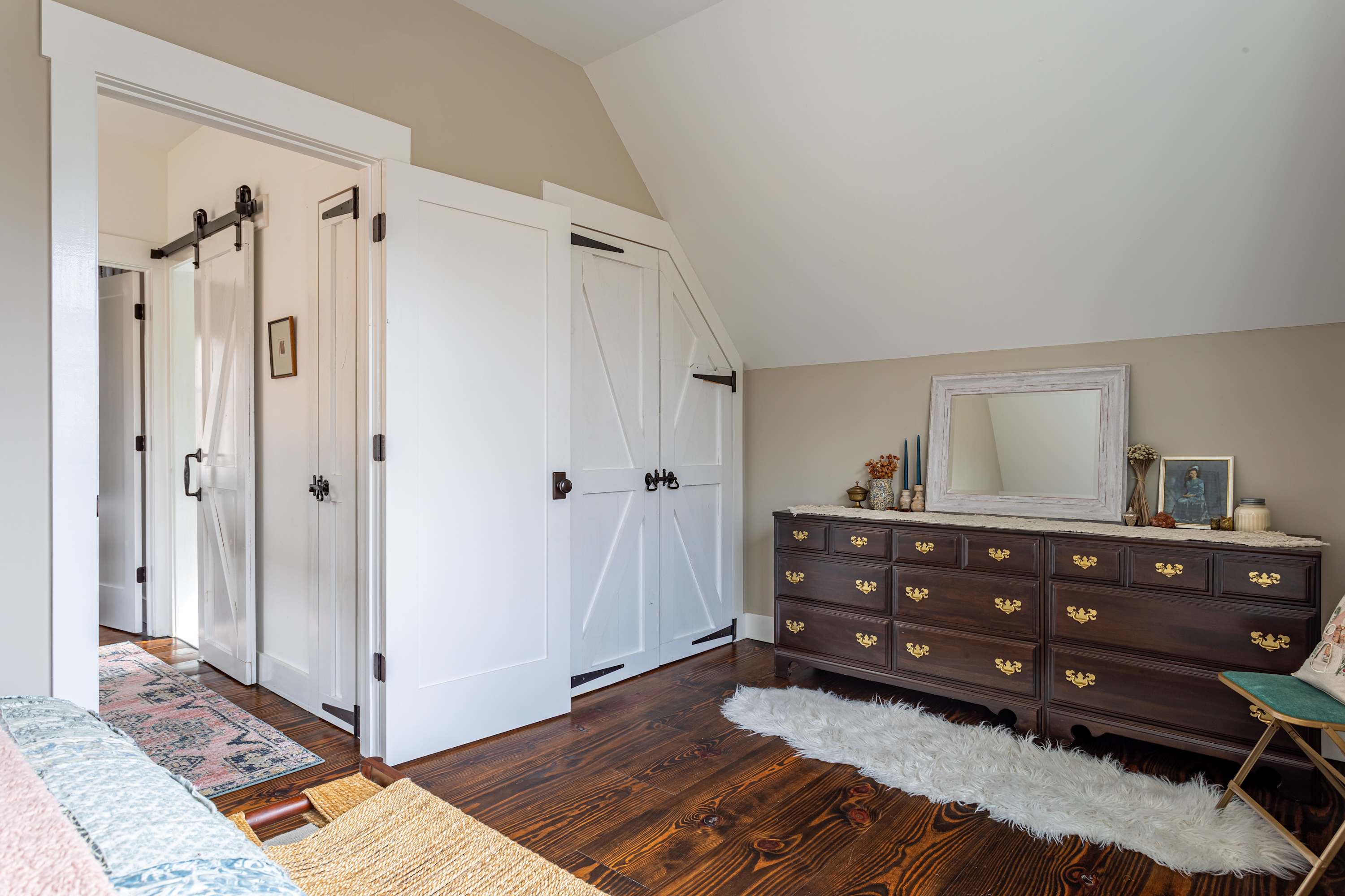 A view from the bedroom highlights two white barn-style doors, one sliding and one hinged, leading to an adjacent room, with dark hardwood floors and a white shag rug in the foreground.
