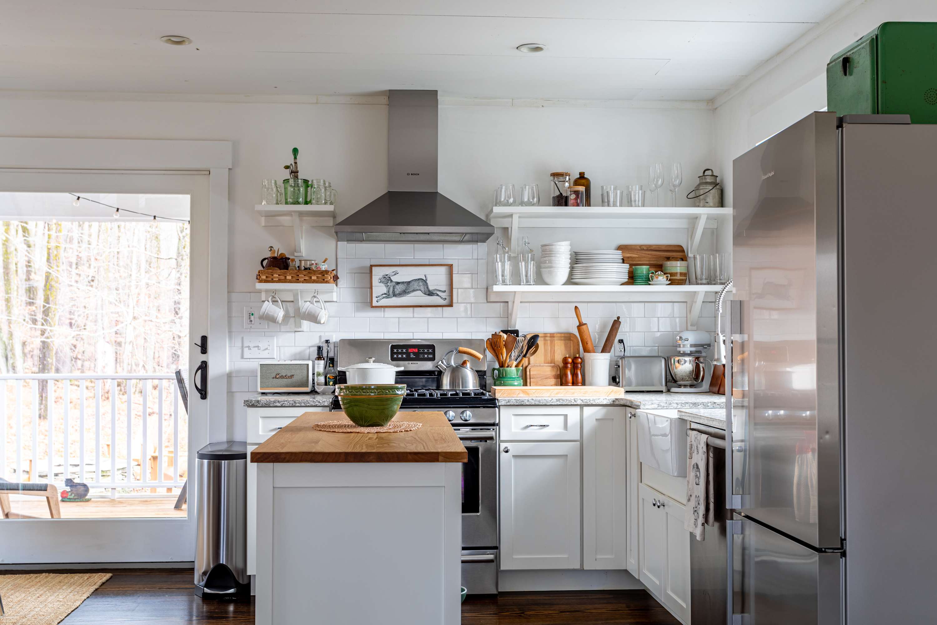 Bright kitchen with white cabinets, granite countertops, a wooden-topped island, stainless steel appliances including a refrigerator and gas range, and open shelving, with a door leading to an outdoor deck.