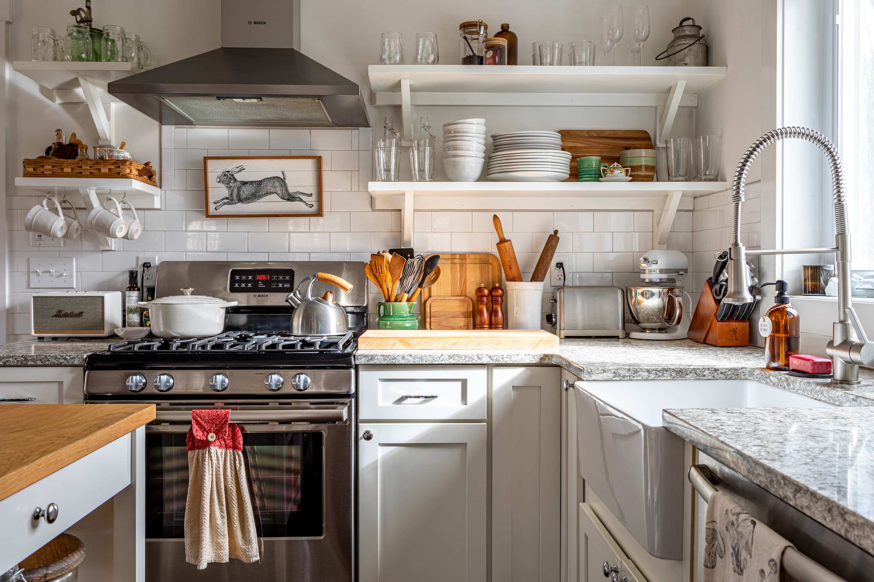 Well-equipped kitchen featuring white subway tile backsplash, open shelves with dishes, stainless steel appliances including a gas range and a farmhouse sink, and granite countertops.