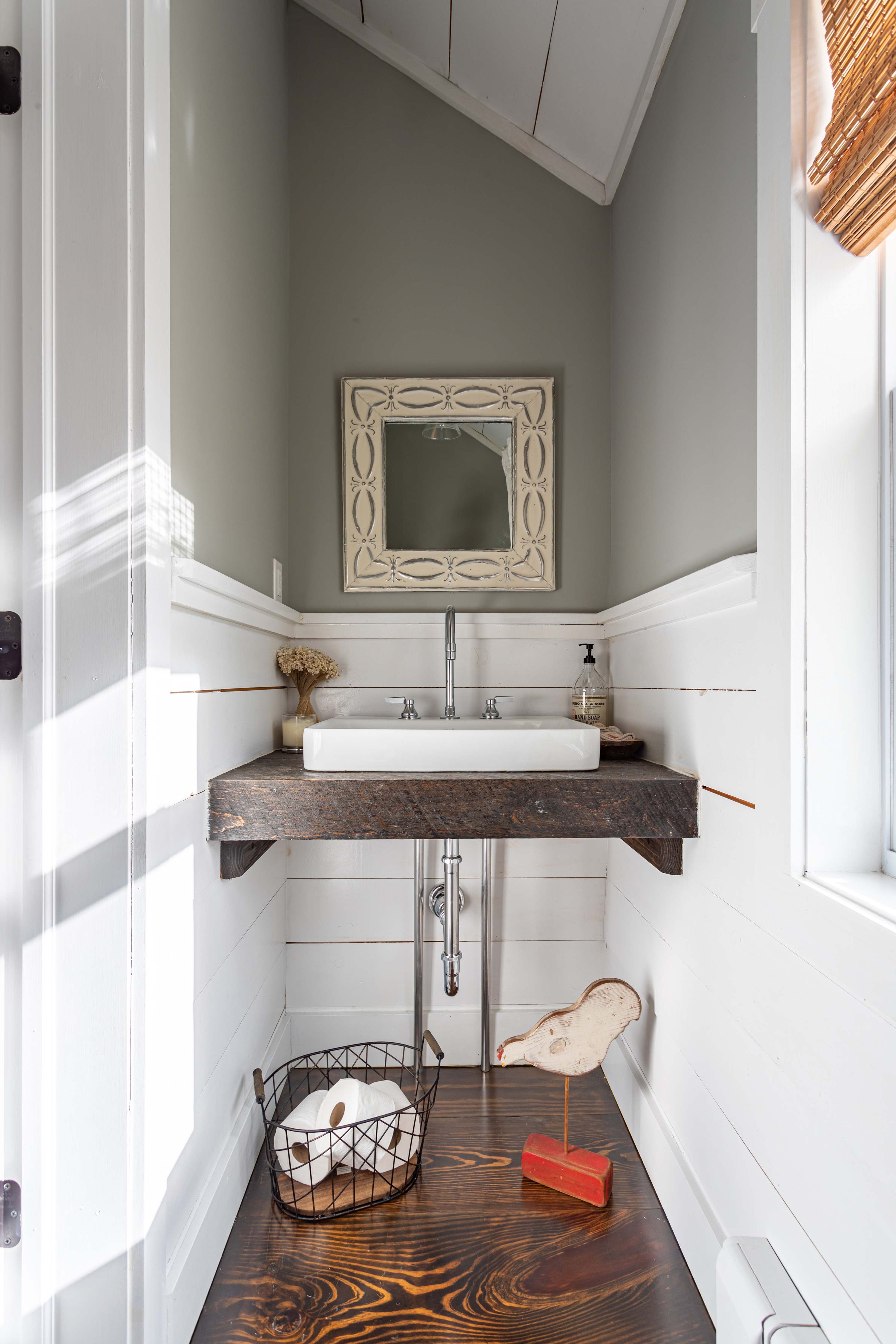 Compact and stylish powder room featuring a vessel sink on a rustic wooden vanity, white shiplap wainscoting, a decorative mirror, and dark wood floors.