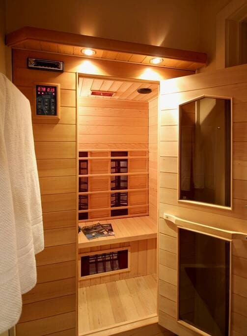 Cozy wooden sauna with light wood paneling, built-in benches, and a digital control panel, illuminated by warm overhead lighting.
