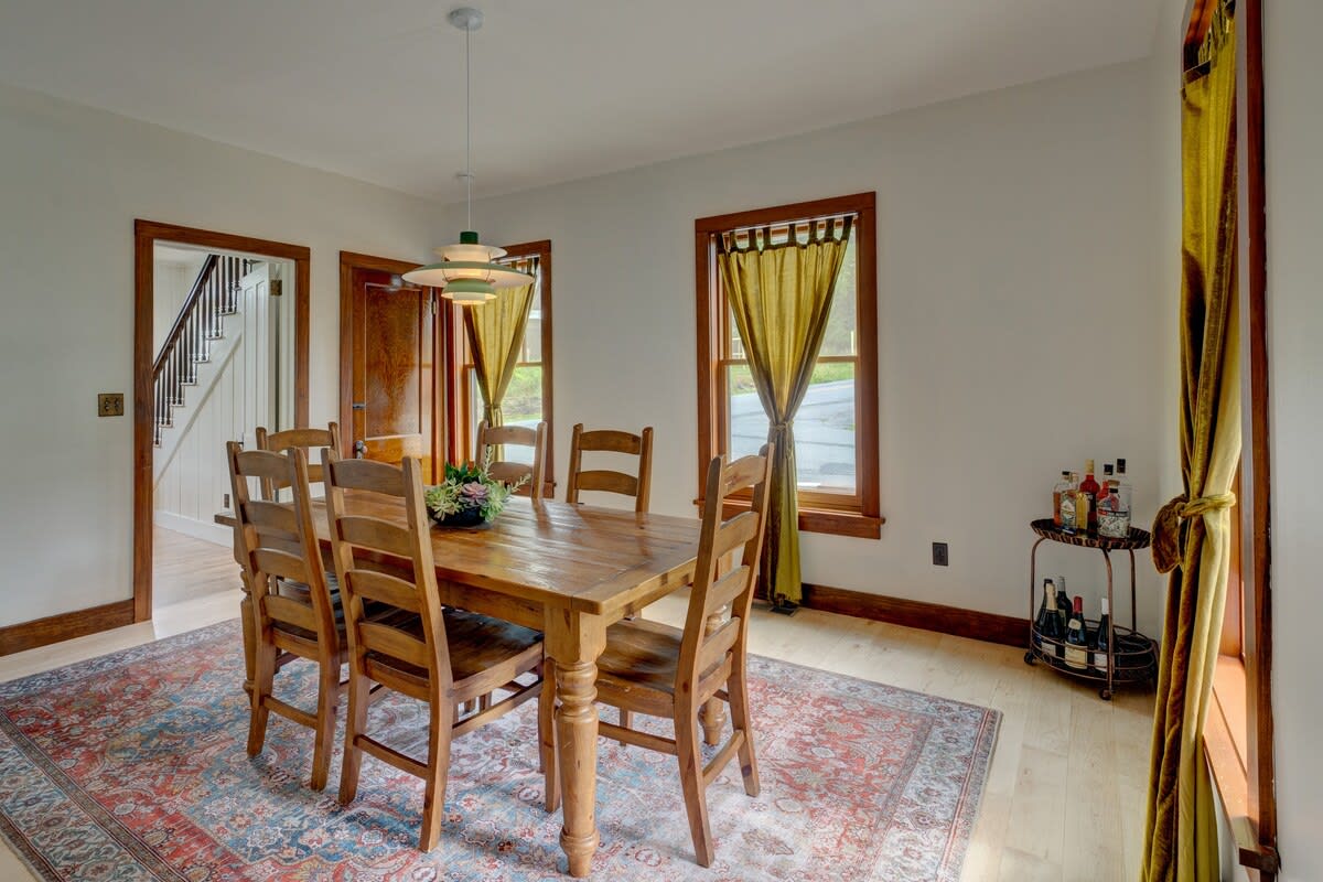 Elegant dining room with a large wooden table and chairs, complemented by a colorful area rug and a modern pendant light. A bar cart is positioned in the corner, and a large framed artwork adorns the wall.