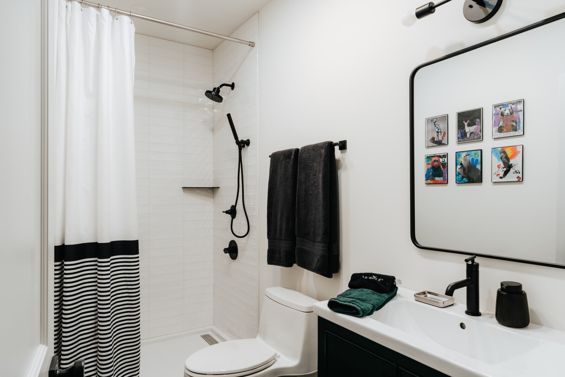 Modern bathroom with a white subway tile shower, black fixtures, a black and white striped shower curtain, and a dark vanity with a white sink and black mirror.
