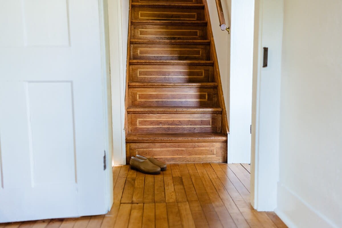 A view of a wooden staircase with intricate detailing on the risers, leading upstairs from a light hardwood floor. White doors frame the entrance to the staircase, creating a welcoming entryway.