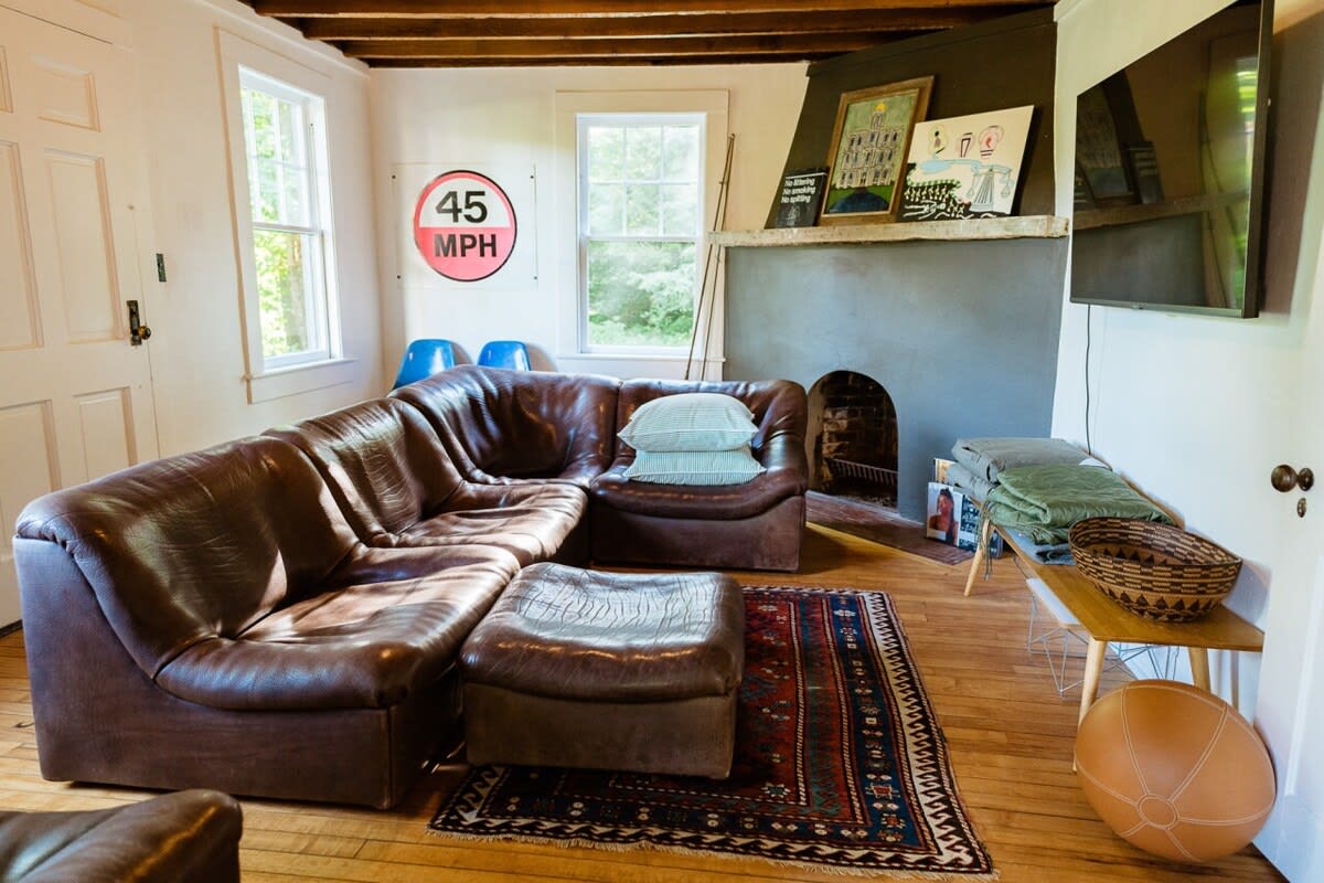 Casual living space with a large brown leather sectional sofa and ottoman, a patterned rug, and a unique fireplace nook, featuring hardwood floors and a wall-mounted TV.