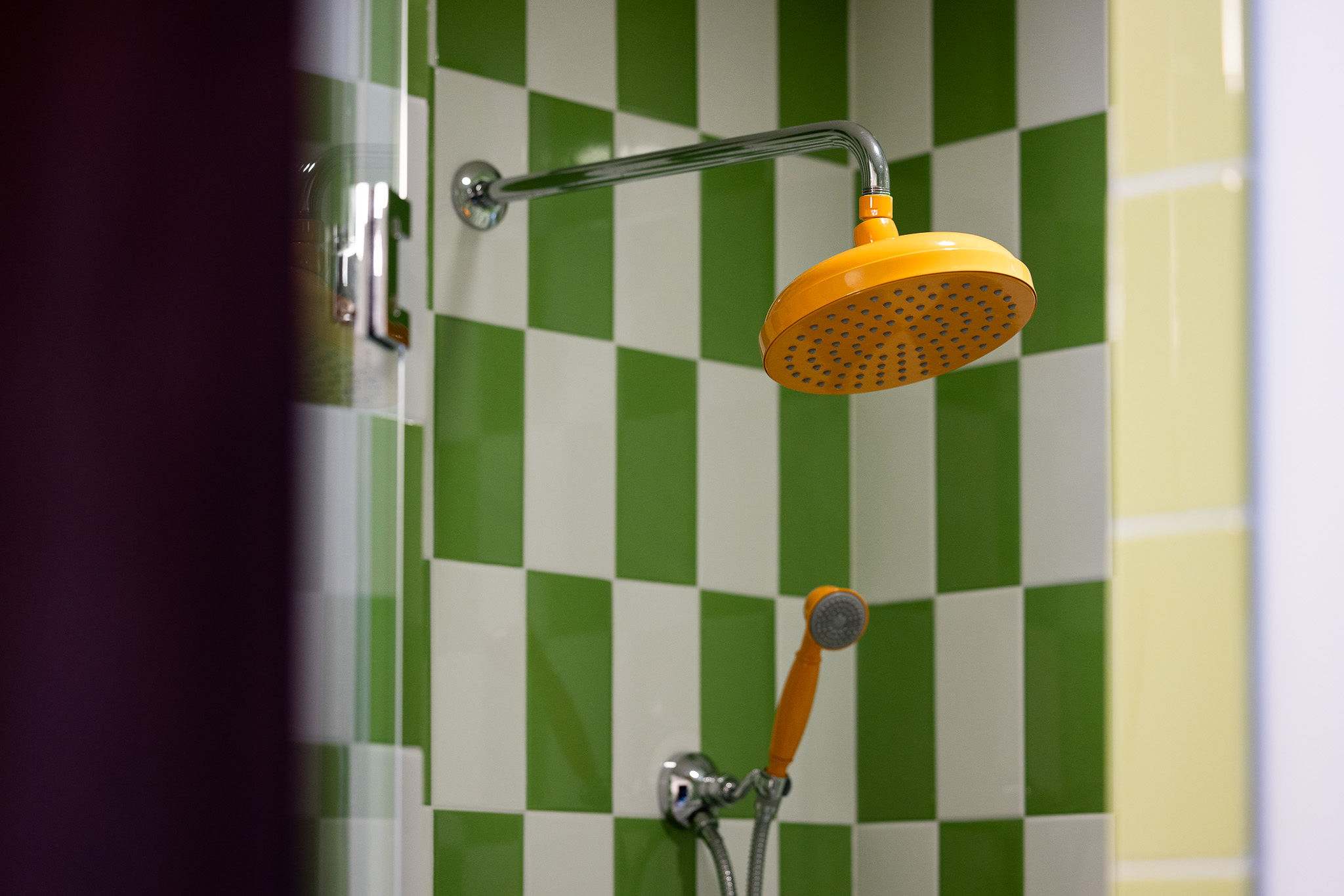 A vibrant shower with green and white checkered tiles, featuring a large yellow rain shower head and a smaller yellow handheld shower head, adding a playful touch to the bathroom.