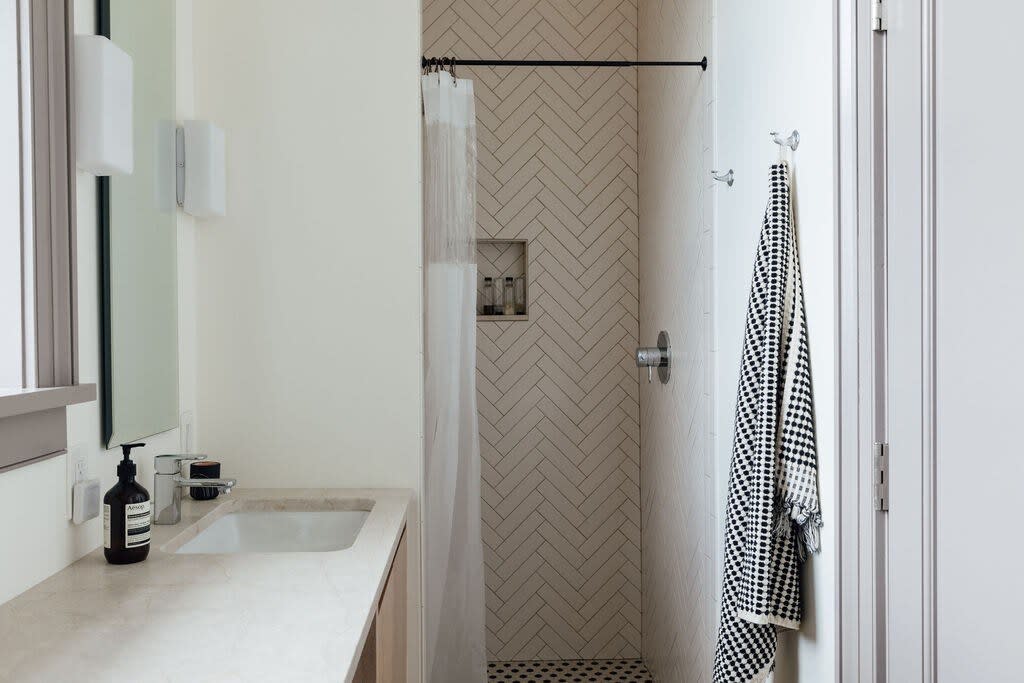 Modern bathroom with a walk-in shower featuring herringbone tile and a black and white patterned towel, alongside a light-colored vanity with a rectangular sink.