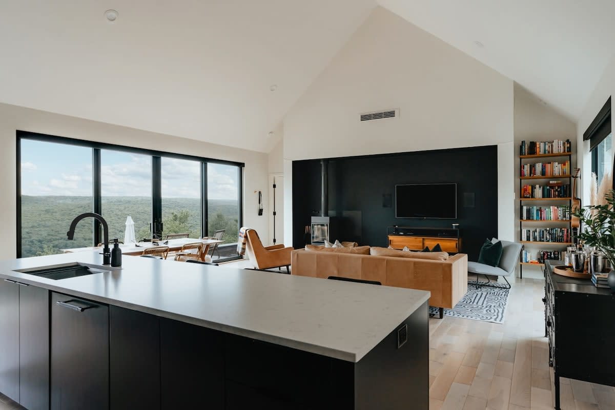 Wide shot of the open-concept kitchen and living area, showcasing the large kitchen island and the spacious living room with multiple seating options and expansive windows. The dining area is also visible.