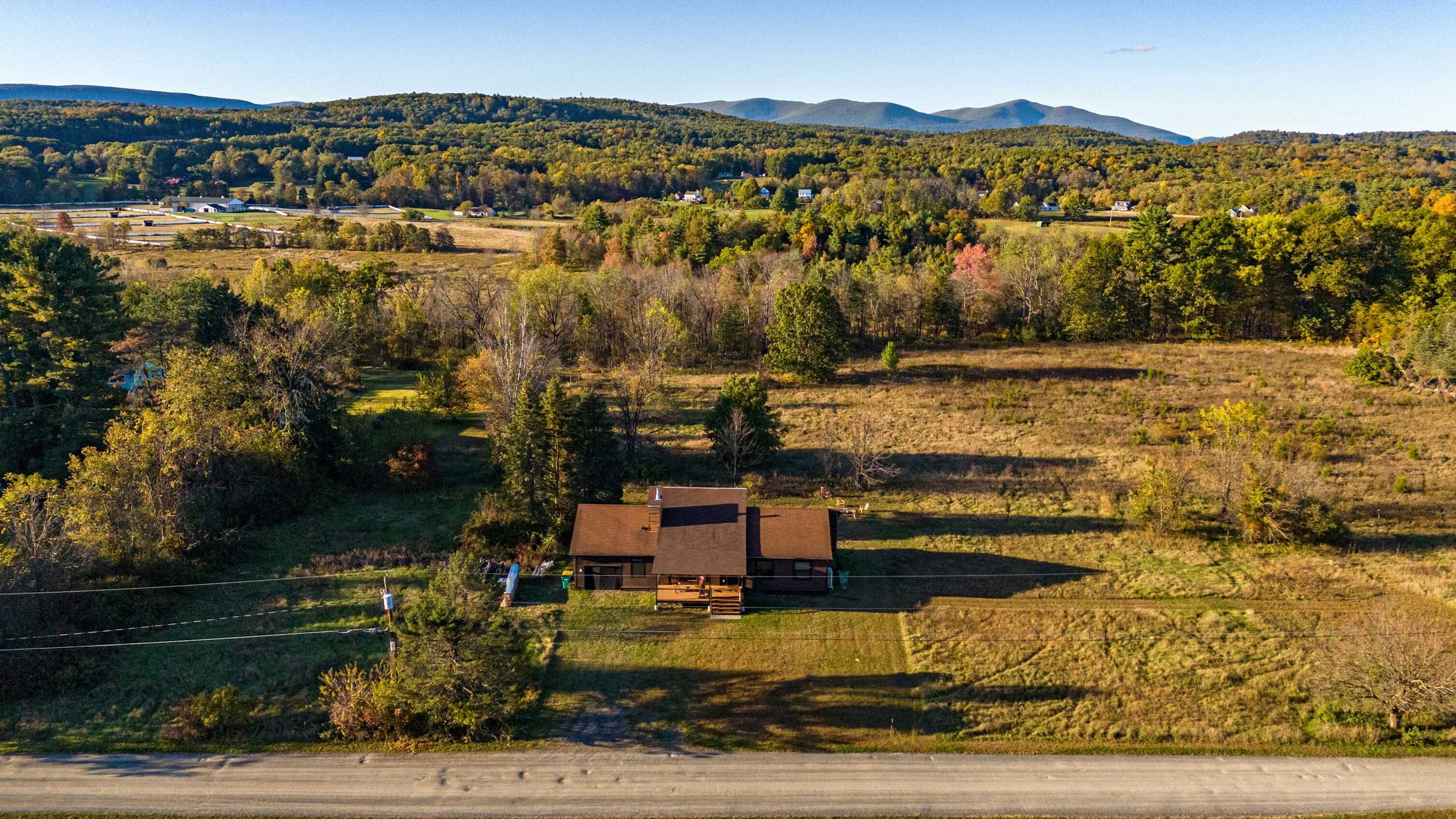 An aerial view of a brown-roofed house nestled in a clearing amidst a vast expanse of autumn trees and rolling hills, showcasing the property's secluded natural setting.