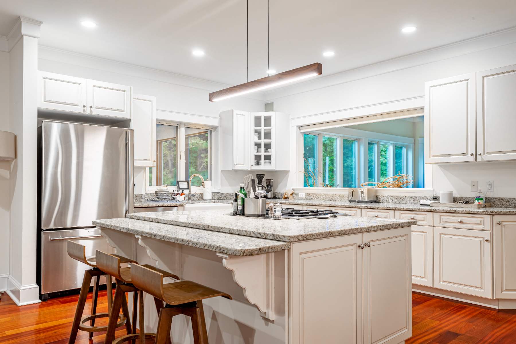 Bright, modern kitchen with white shaker cabinets, granite countertops, and stainless steel appliances, including a large island with bar seating and a gas range, illuminated by recessed lighting.