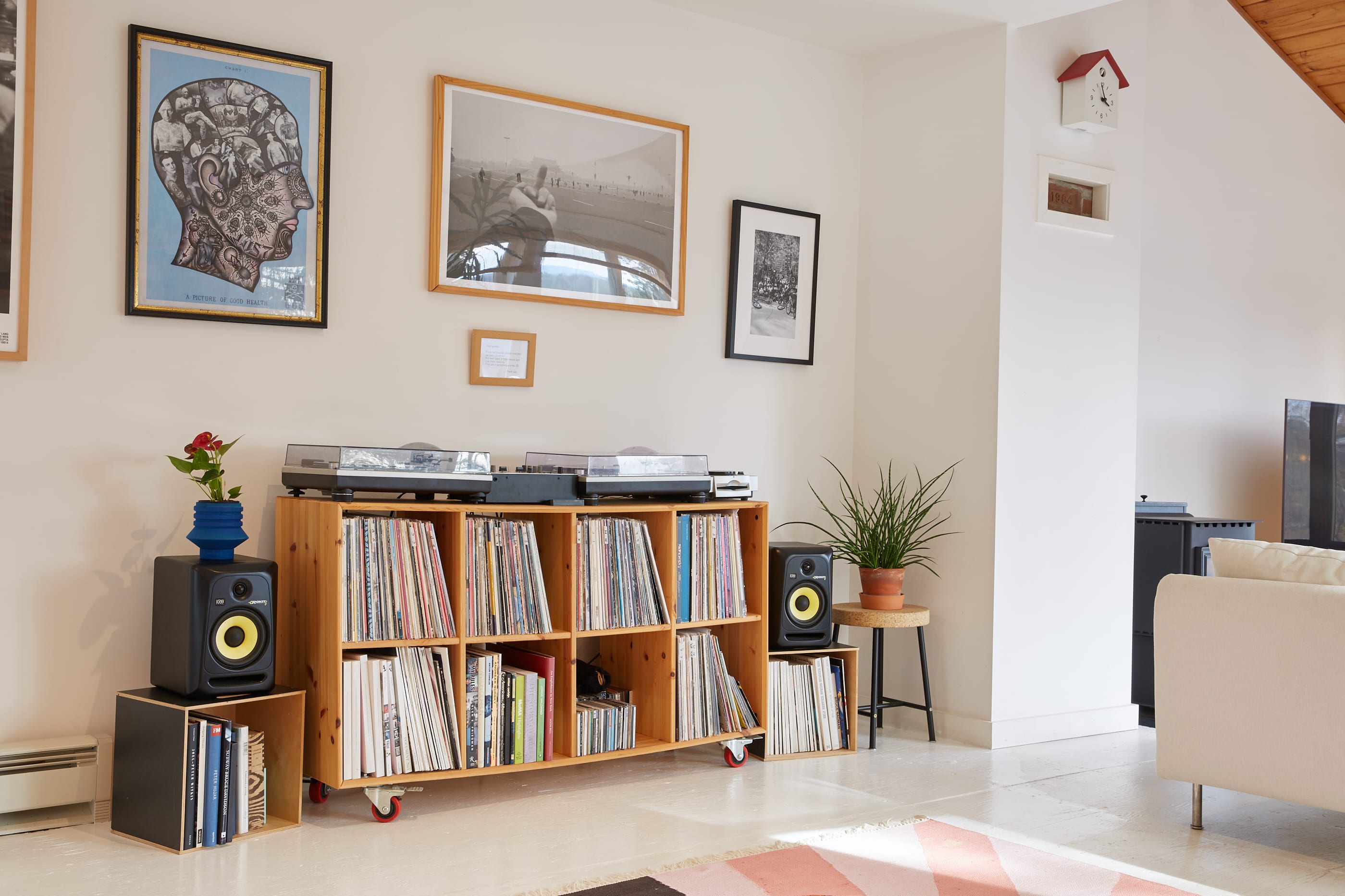A corner of a living room dedicated to music, featuring a wooden record player console with extensive vinyl storage, two turntables, and speakers, complemented by framed artwork on the wall.