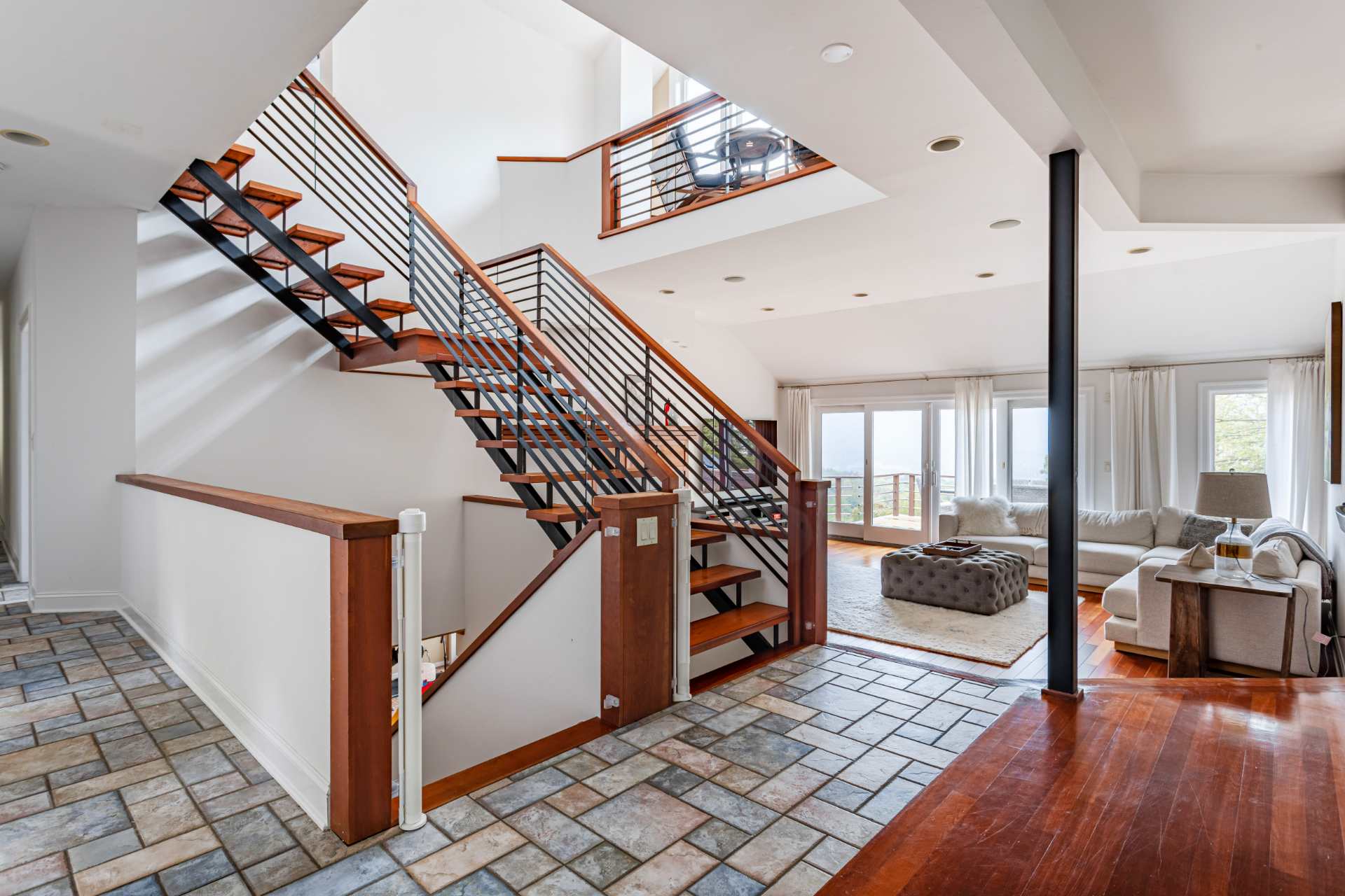 Spacious open-concept living area featuring a modern wooden staircase with black metal railings, leading to upper levels, and a cozy living room with a large sectional sofa.