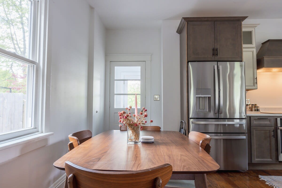 Another perspective of the dining area, highlighting the rich wooden dining table and chairs. The stainless steel French door refrigerator and kitchen cabinetry are prominently featured in the background.