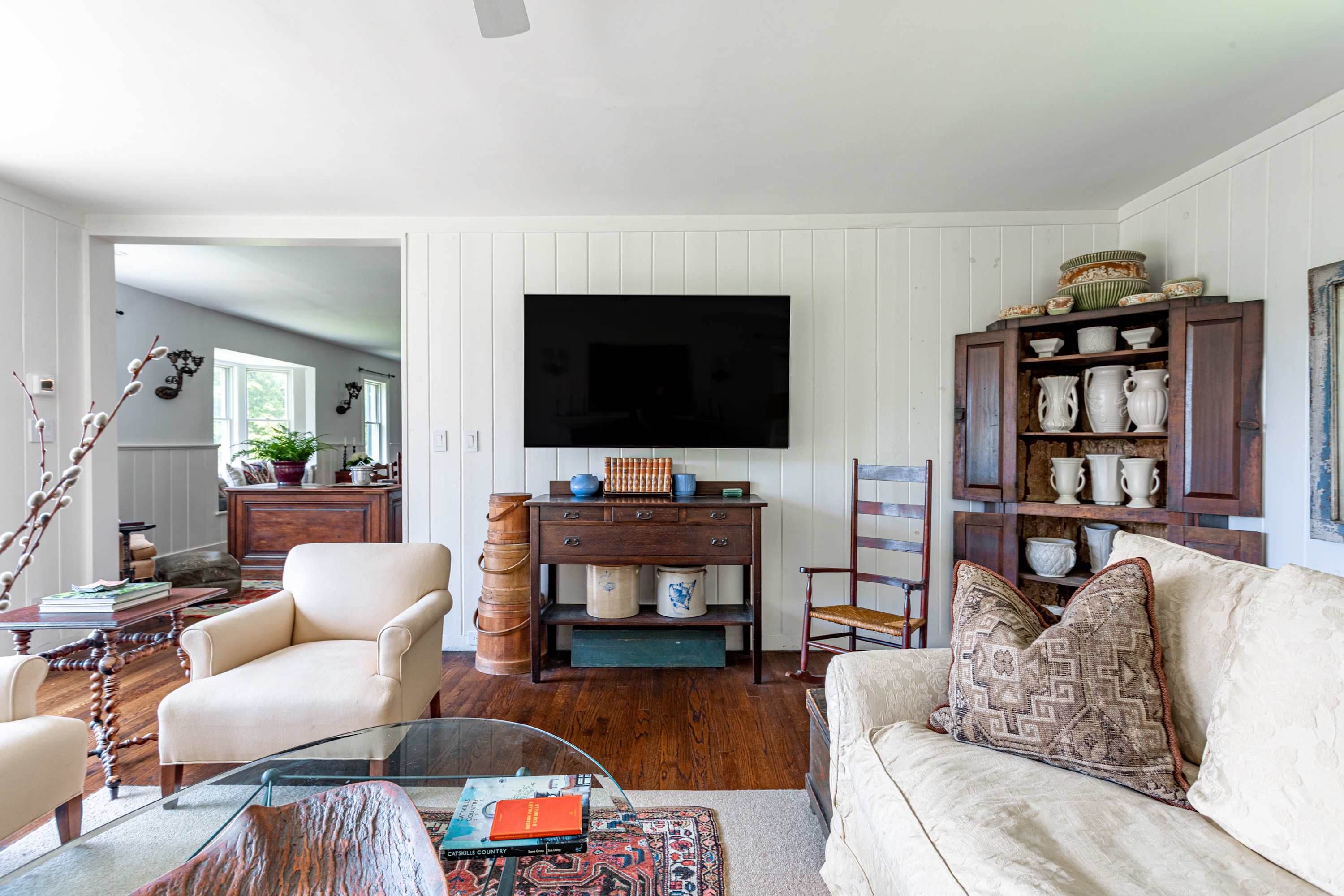 A view of the living room showing a wall-mounted TV above a wooden console table, a cream sofa, and a dark wood cabinet filled with decorative items, all on dark hardwood floors.