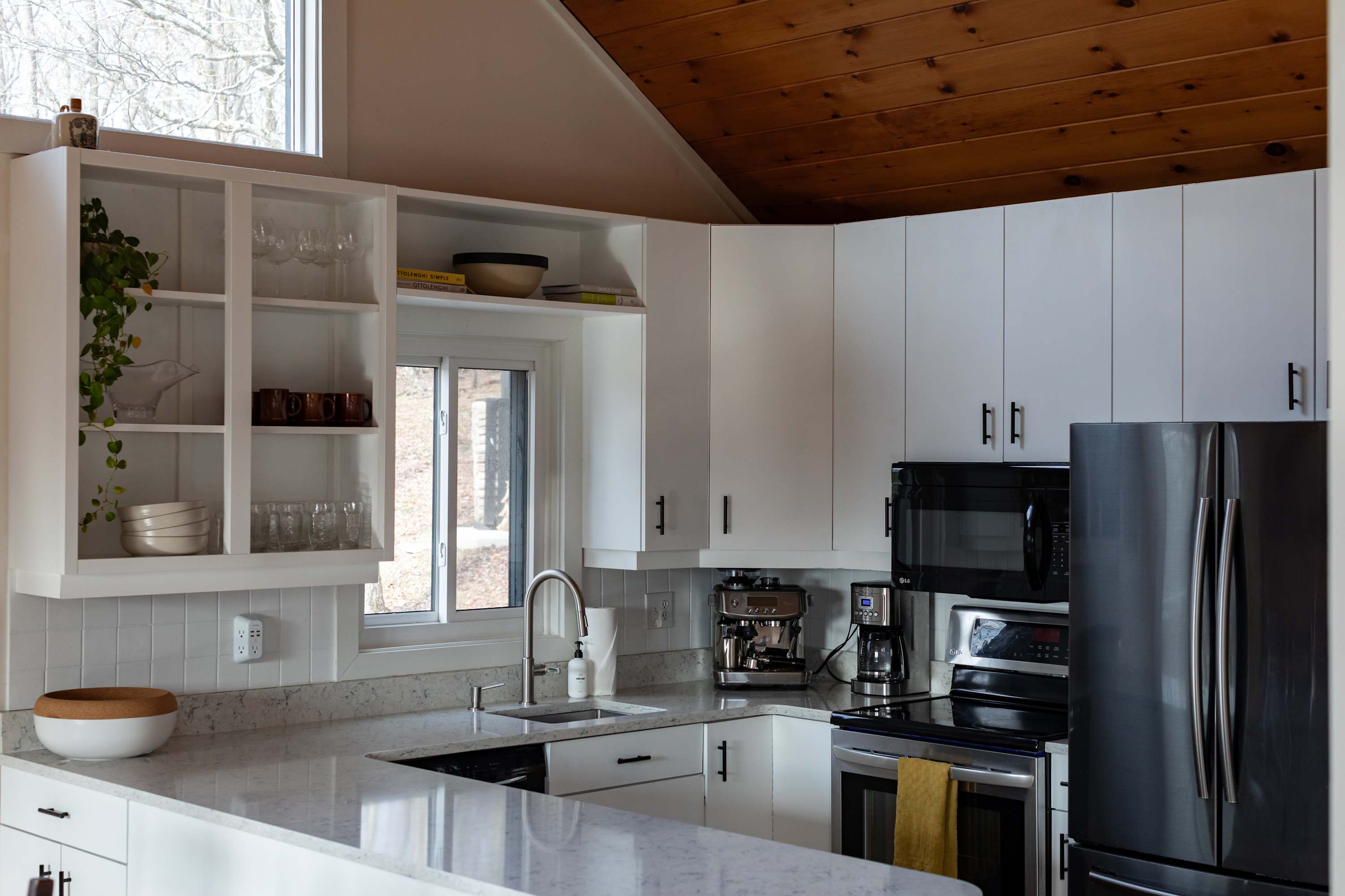 An expansive view of the modern kitchen reveals white shaker cabinets, light quartz countertops, and stainless steel appliances including a refrigerator, microwave, and stove, with a coffee station.