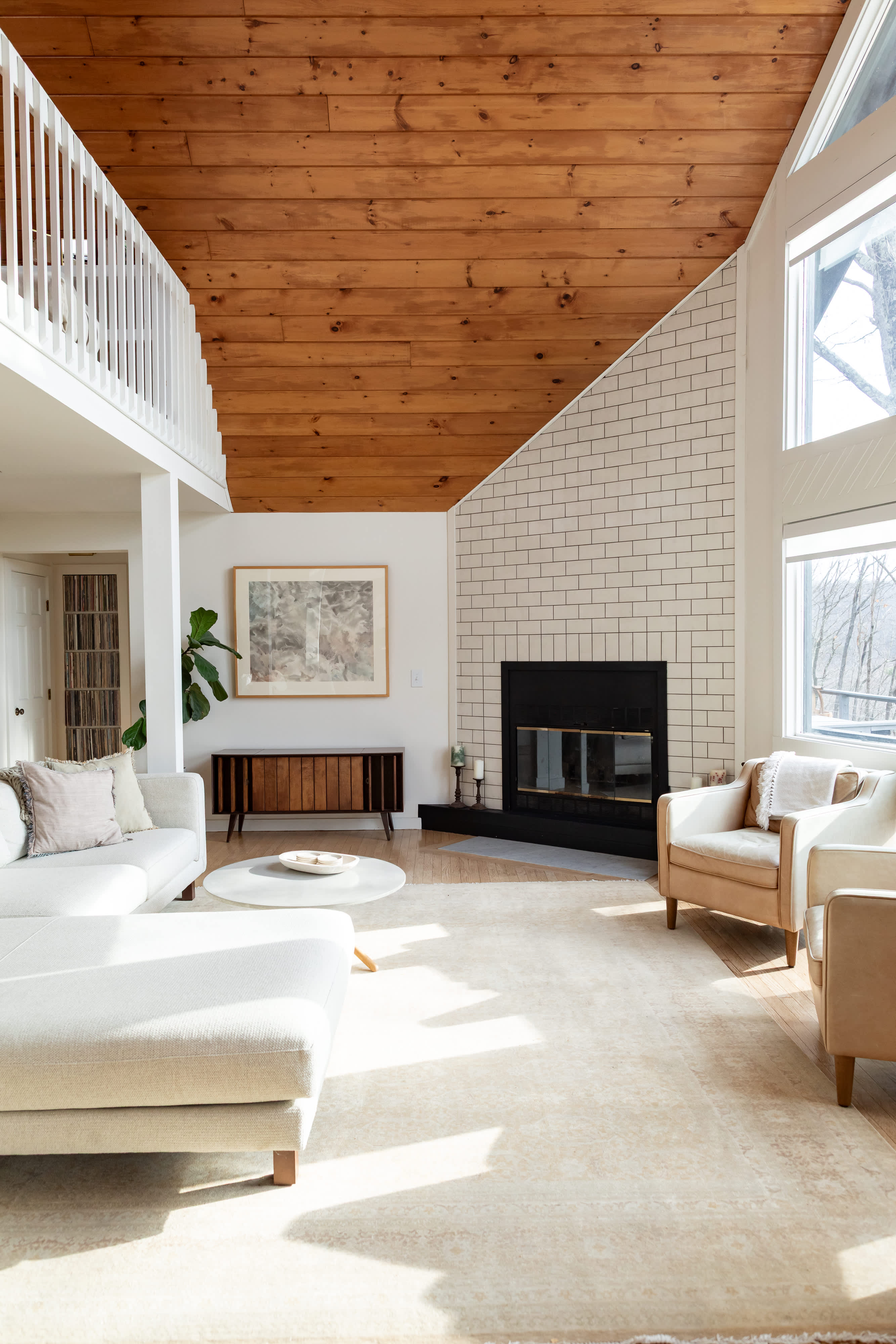 The expansive living room showcases a dramatic vaulted wooden ceiling, a cozy fireplace with subway tile, a large sectional sofa, and two armchairs, with a staircase leading to an upper level.