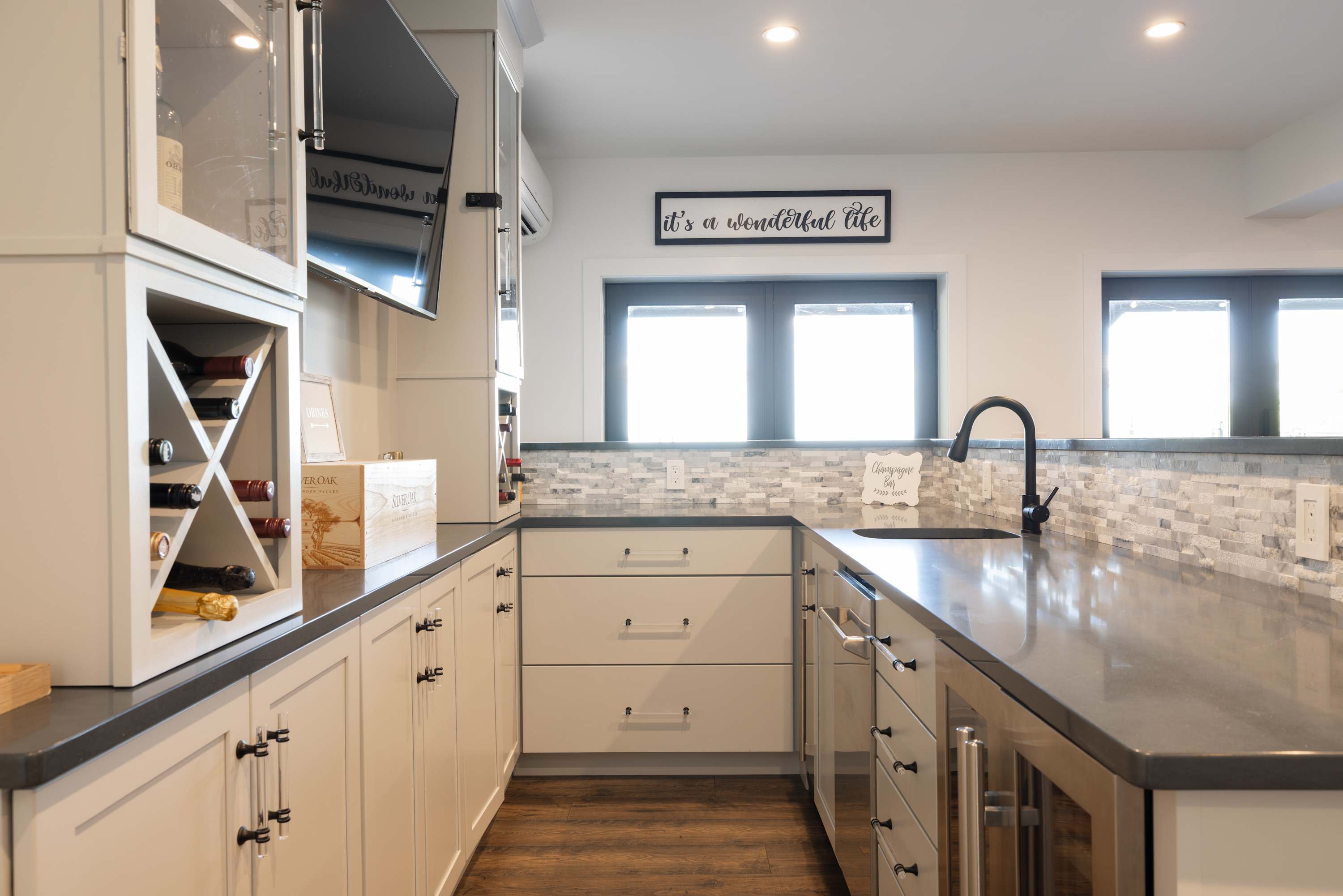 Compact kitchenette with white shaker cabinets, dark countertops, a white subway tile backsplash, and a black gooseneck faucet, featuring a small window above the sink.