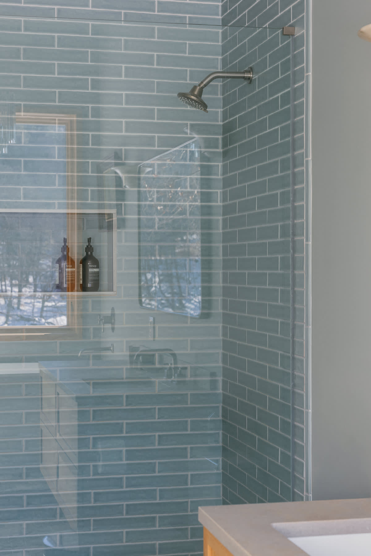 Contemporary shower with light blue subway tiles, a glass enclosure, and a built-in niche, reflecting the snowy outdoor view from a nearby window.