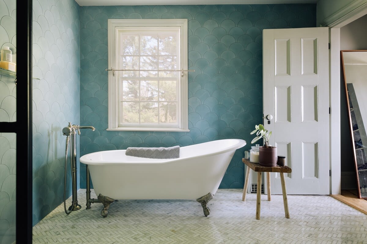 A bright bathroom featuring a classic white clawfoot bathtub with vintage-style fixtures, surrounded by walls adorned with blue scalloped tiles and a white herringbone tile floor.