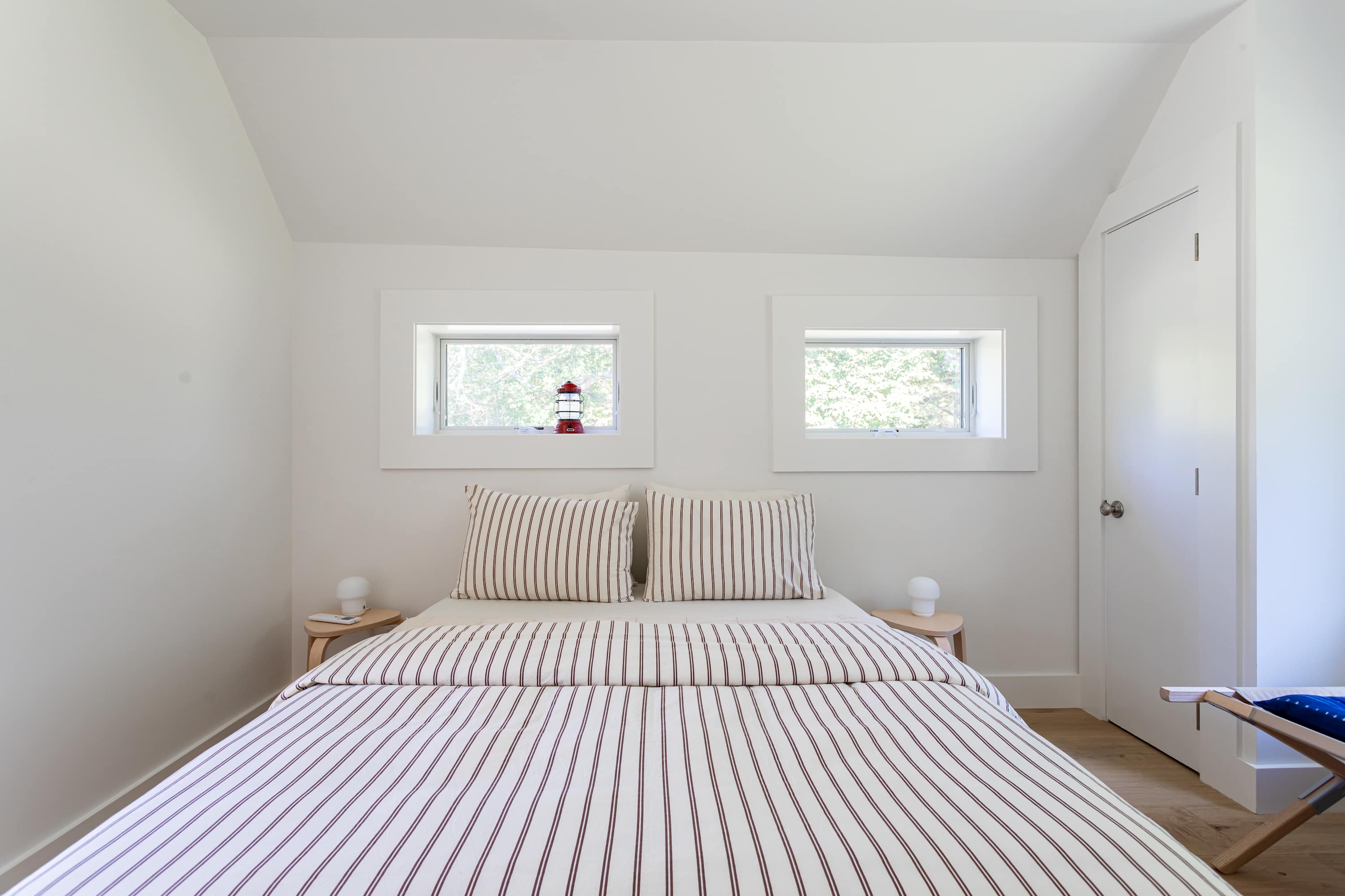 Inviting bedroom with a bed featuring striped bedding and two small windows above the headboard, adorned with a decorative red lighthouse.
