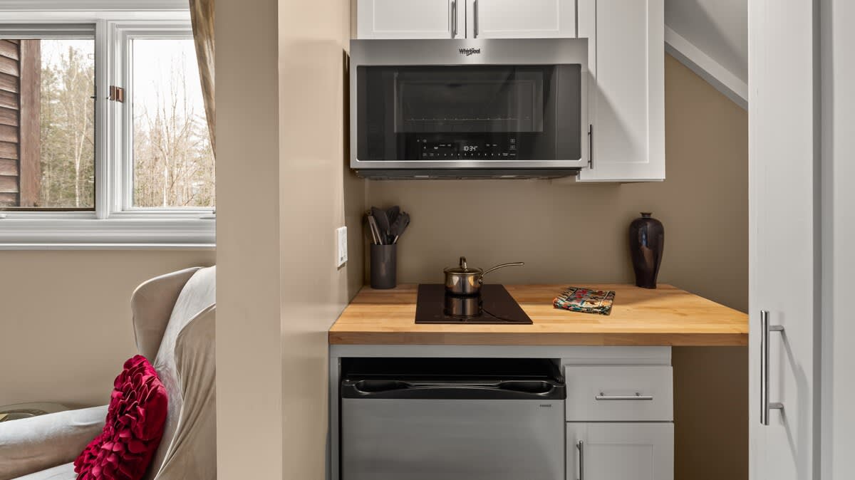 A compact kitchenette area featuring a built-in microwave above a wooden countertop with a small induction cooktop and a mini-fridge below. White upper cabinets provide storage.