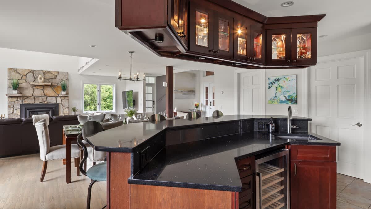 A spacious kitchen island with a black granite countertop and integrated sink serves as a bar area with a wine fridge, connecting to the dining space and offering a glimpse into the living room beyond.