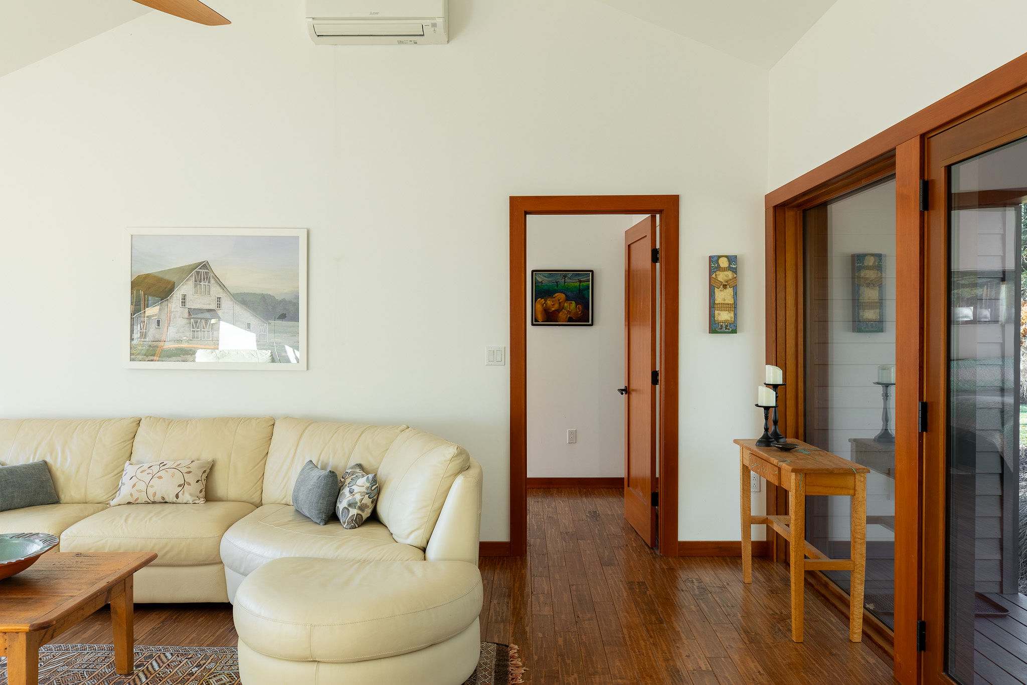 A corner of the living room showing a light leather sectional sofa, a wooden console table with decor, and a doorway leading to another room, all under a vaulted ceiling.